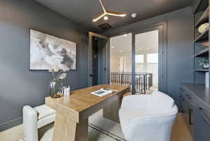 Dedicated office space featuring a built-in shelving unit, custom cabinetry, modern lighting fixture, wood-finish flooring, and glass-paneled double doors