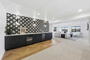 Open-concept entertainment space featuring a patterned tile accent wall, built-in cabinetry with integrated beverage coolers, and warm wood-finish flooring