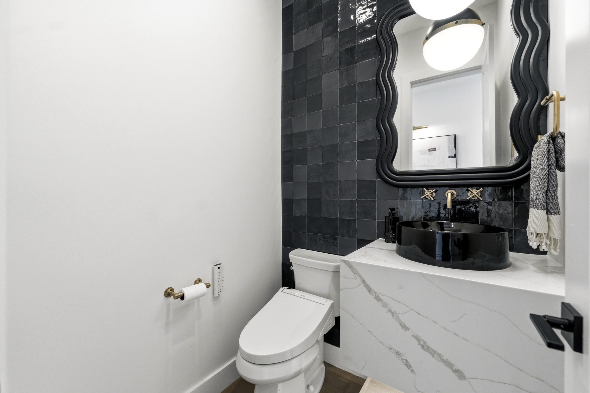 Modern powder room featuring a black vessel sink, gold-finish wall-mounted faucet, and a sleek, white toilet