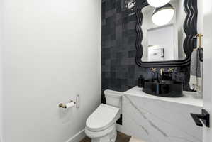 Modern powder room featuring a black vessel sink, gold-finish wall-mounted faucet, and a sleek, white toilet
