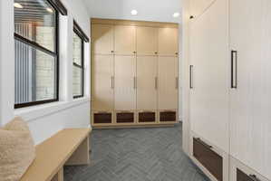 Hallway featuring extensive built-in cabinetry with modern hardware, grey herringbone-patterned tile flooring, a built-in bench, and multiple windows