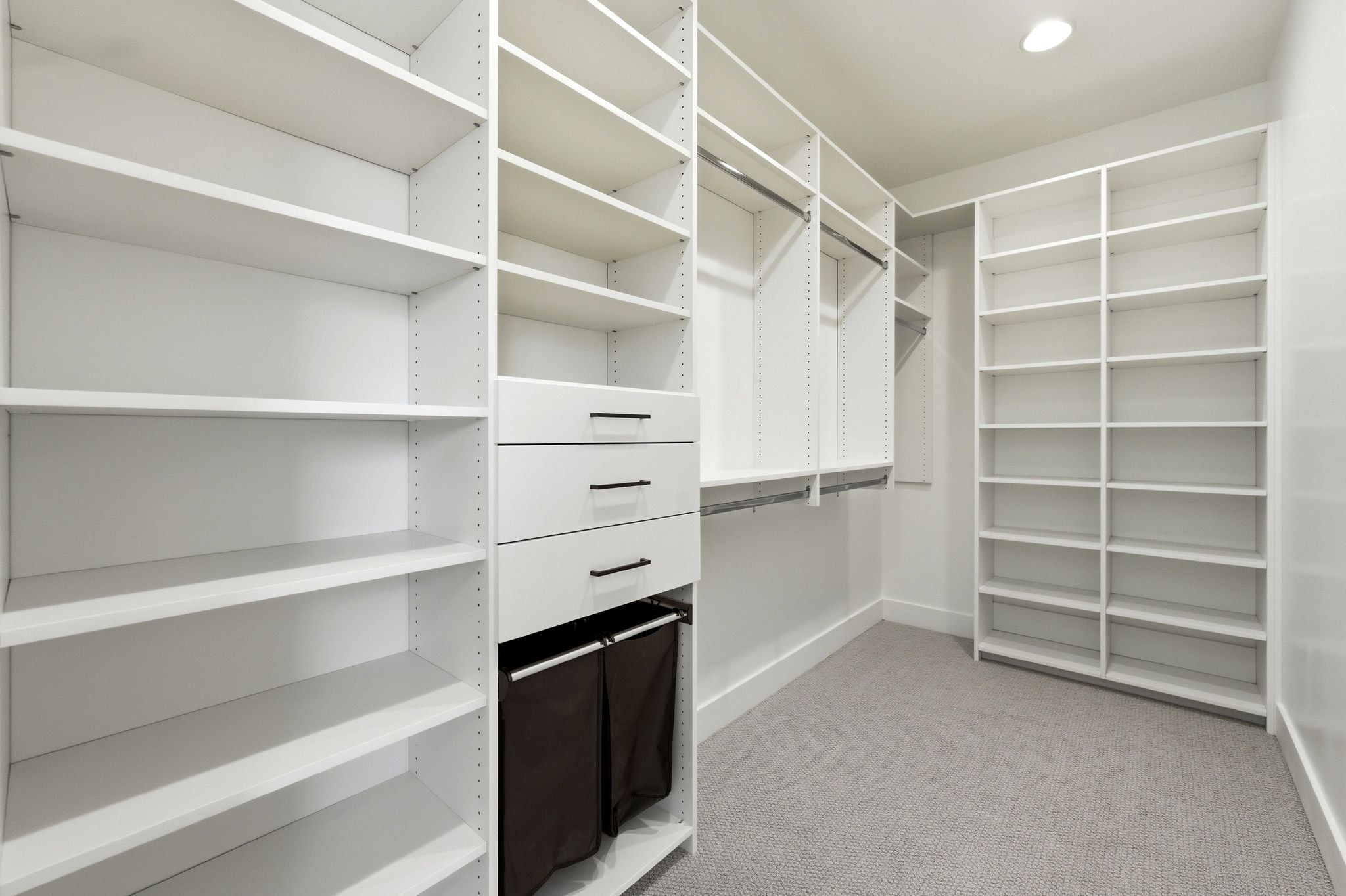 Custom closet system featuring extensive shelving, multiple hanging rods, built-in drawers with modern pulls, recessed lighting, and soft carpet flooring
