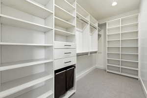 Custom closet system featuring extensive shelving, multiple hanging rods, built-in drawers with modern pulls, recessed lighting, and soft carpet flooring