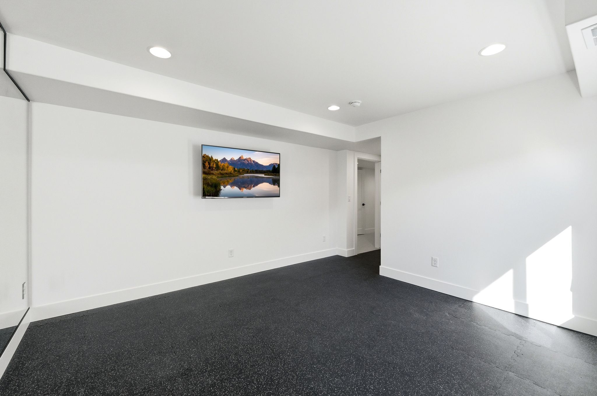 Spacious room featuring dark rubber flooring, white baseboards, recessed lighting, and a large wall-mounted mirror