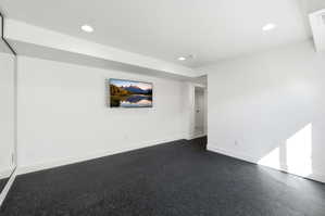 Spacious room featuring dark rubber flooring, white baseboards, recessed lighting, and a large wall-mounted mirror