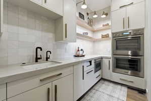 Modern kitchen featuring a built-in sink with matte black fixtures, crisp white cabinetry with bronze hardware, and a white square-tiled backsplash