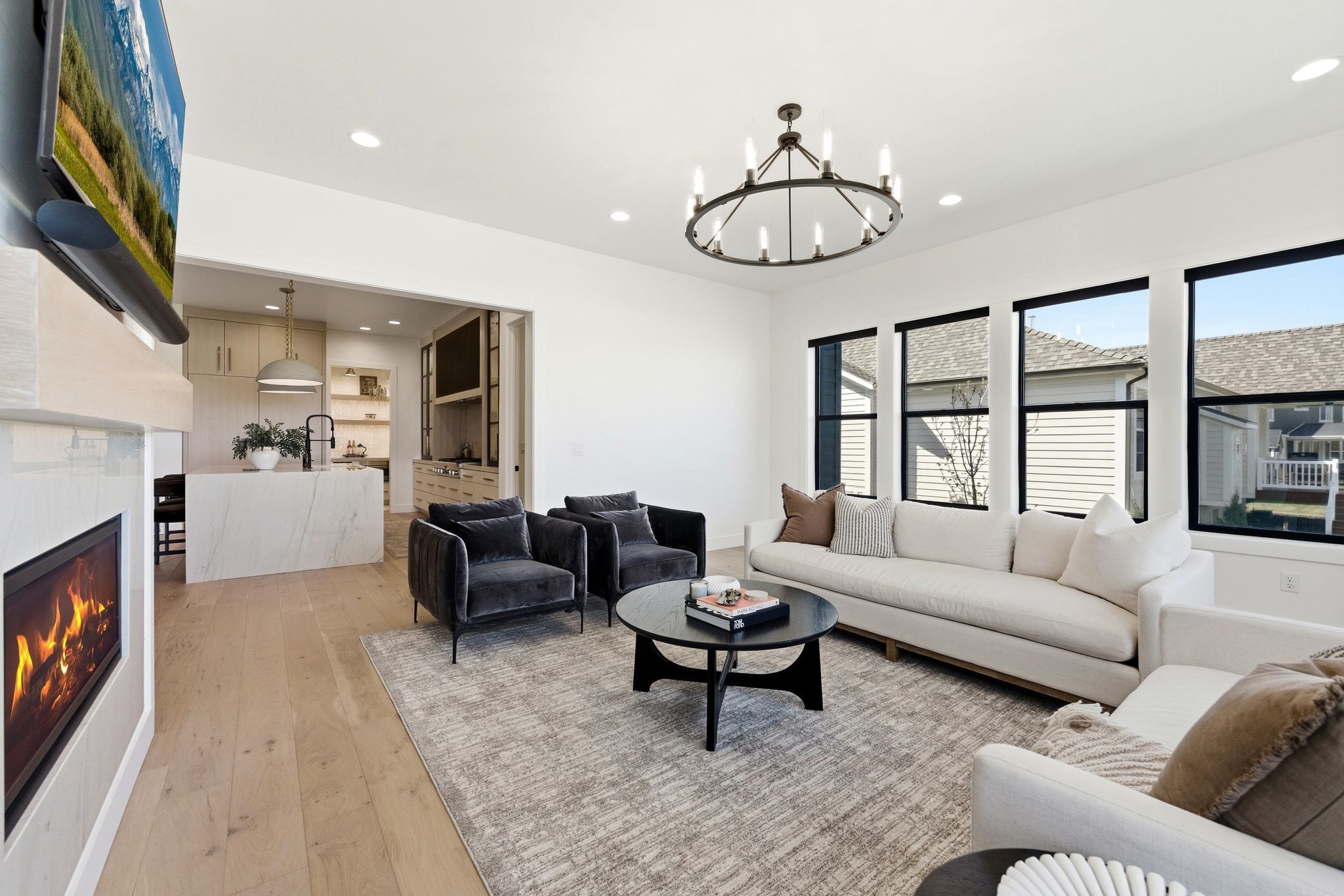 Spacious living area featuring light wood-finish flooring, a contemporary fireplace with a stone surround, and recessed lighting