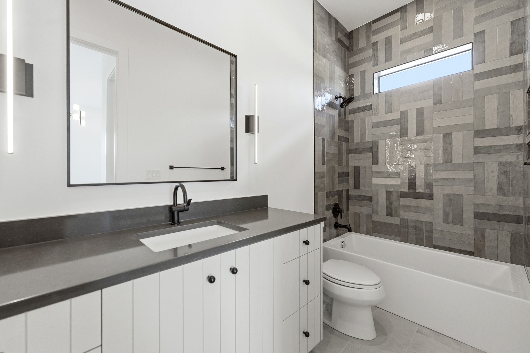 Bathroom featuring a white vanity with paneling, dark countertop, and matte black fixtures