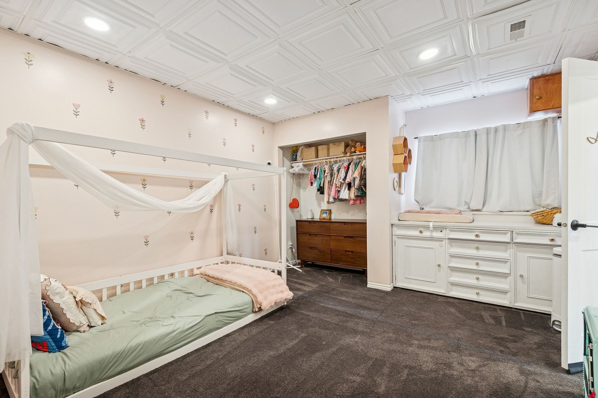 Recessed lighting illuminates the textured ceiling paneling and soft patterned wallpaper