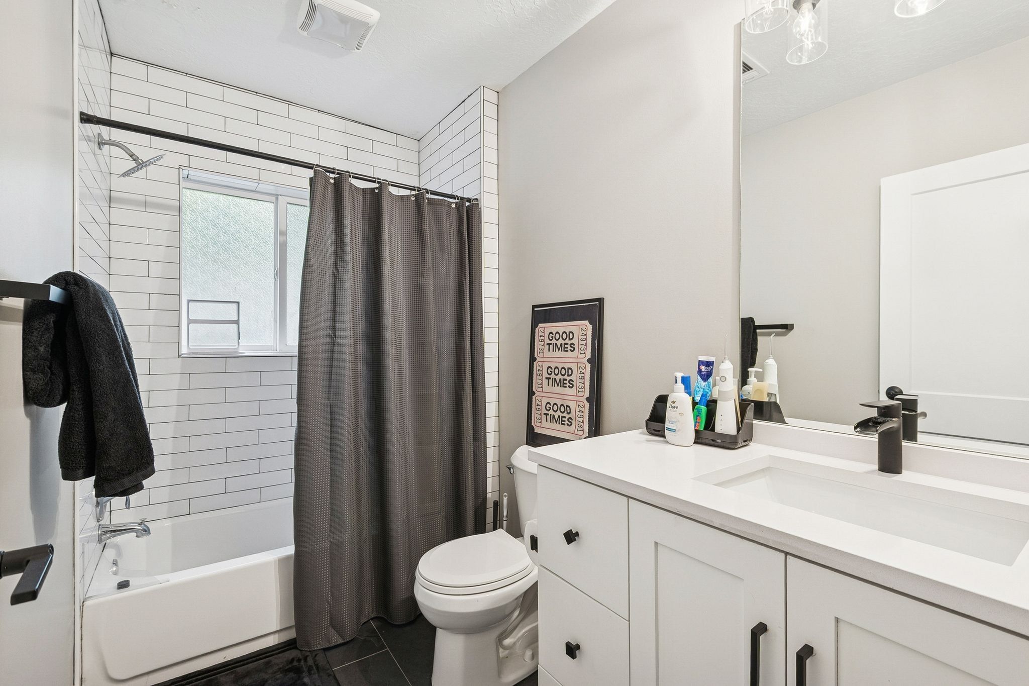 Bathroom featuring a white subway tile shower surround with a window, a white vanity with an integrated sink, a large wall-mounted mirror, and black hardware