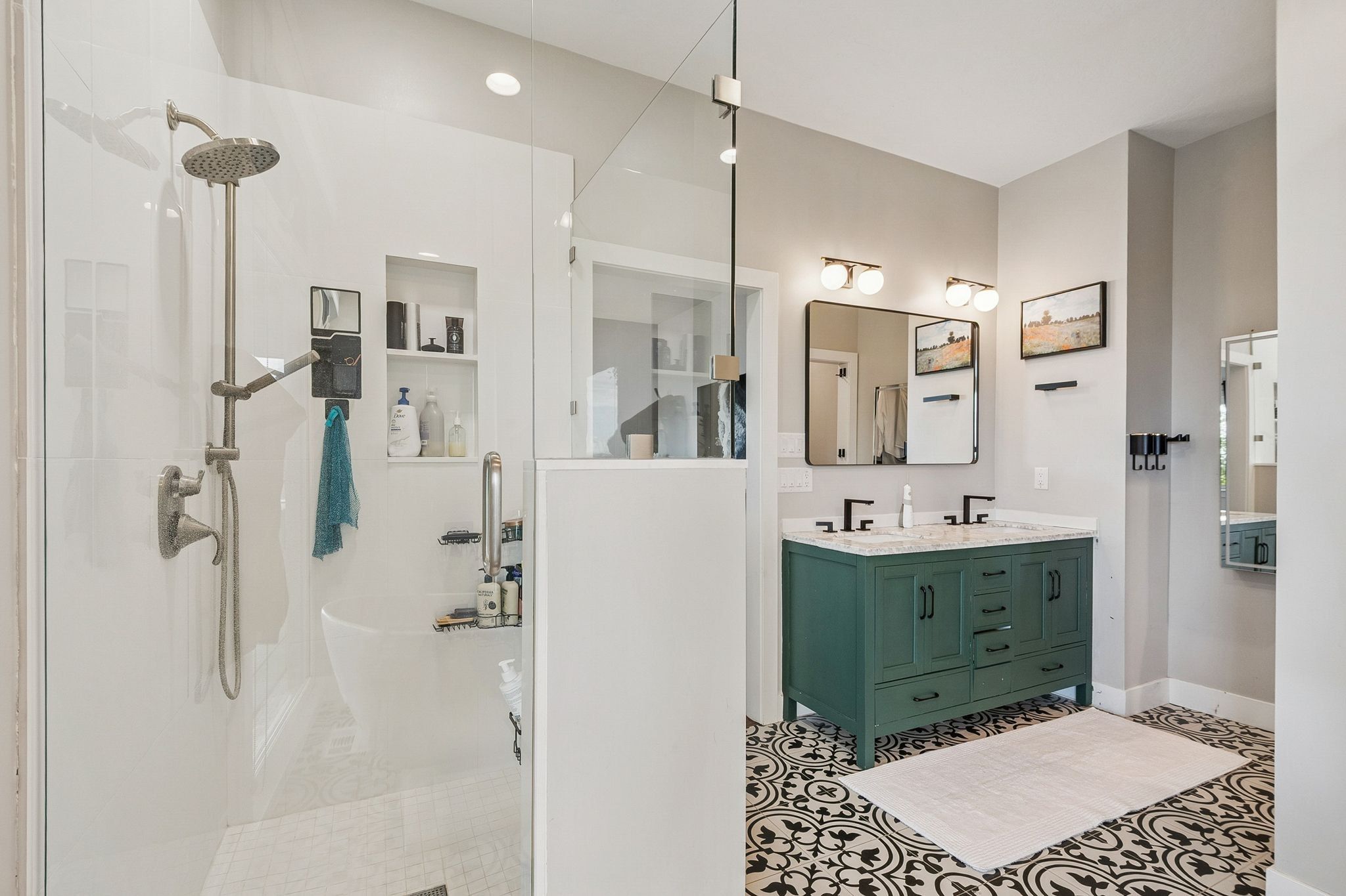 Spacious bathroom featuring a frameless glass shower enclosure, dual vanity with a green cabinet base and stone-finish countertop, black fixtures, and patterned floor tile