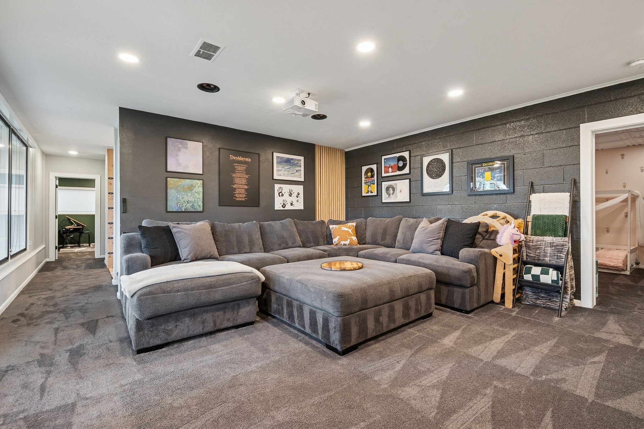 Carpeted recreation room featuring recessed lighting, a built-in projector, dark accent walls, and a large window providing ambient light