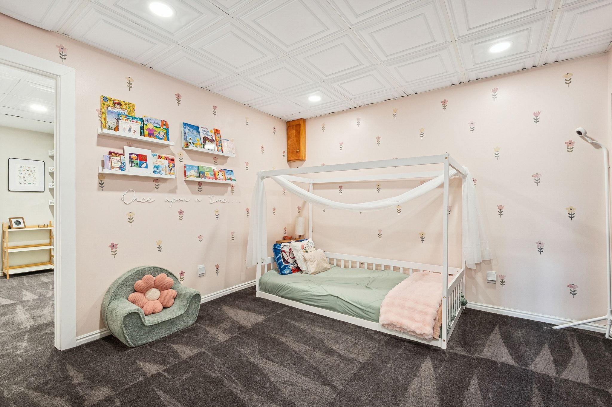 Recessed lighting illuminates a room featuring patterned wall coverings, a detailed ceiling with square panels, and dark patterned carpeting