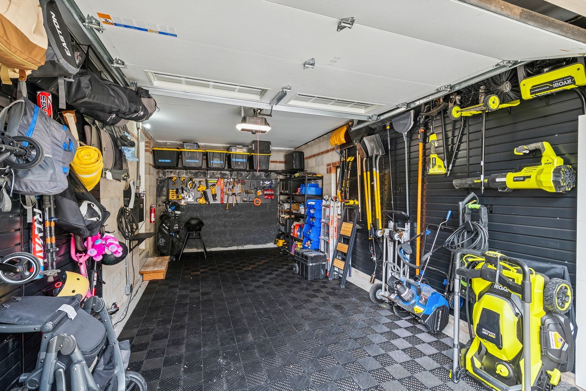 Garage space featuring checkerboard pattern flooring, slatwall organization systems, overhead lighting, and built-in shelving