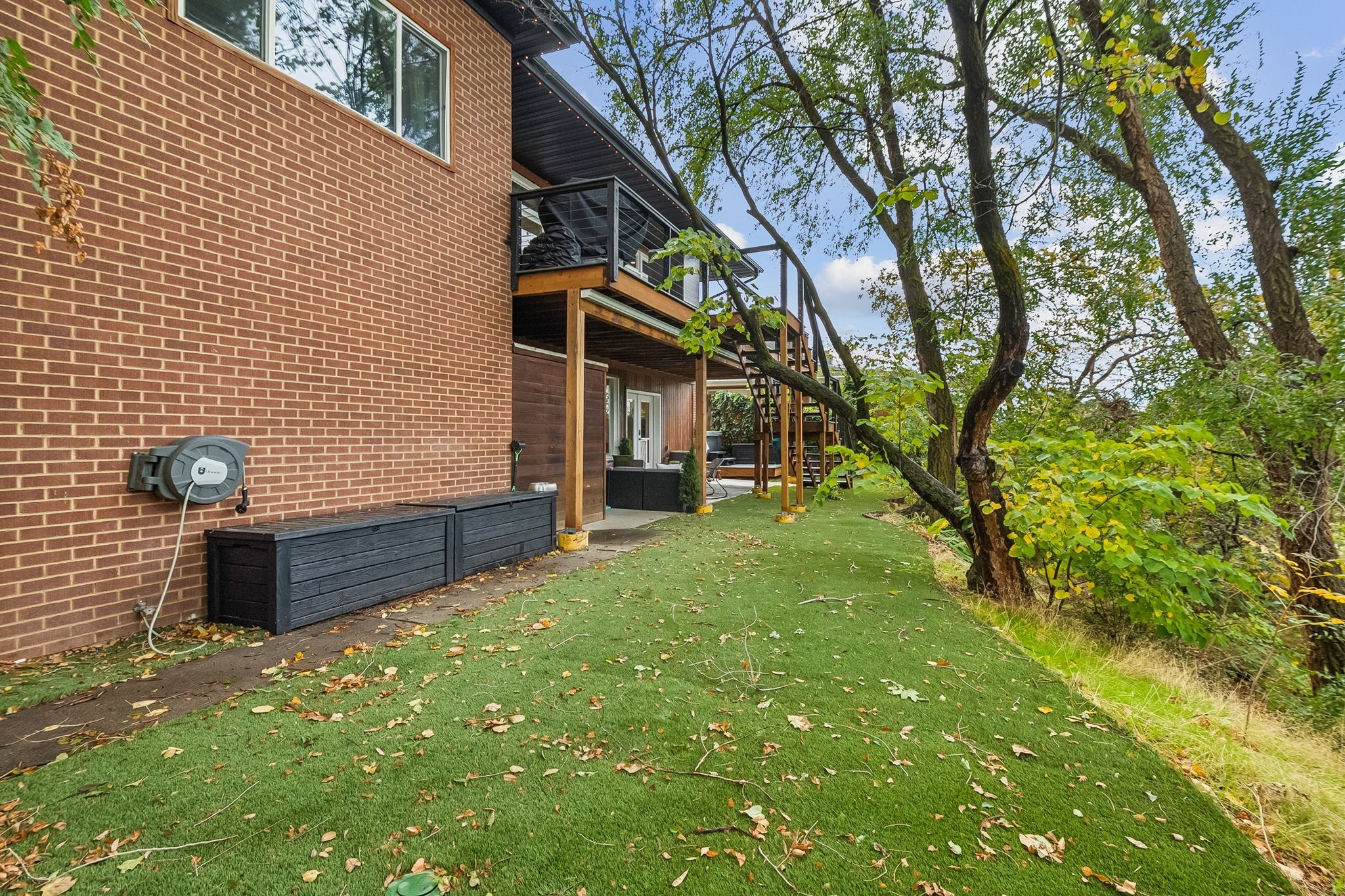 Terraced landscaping with artificial turf, bordered by mature trees and natural foliage