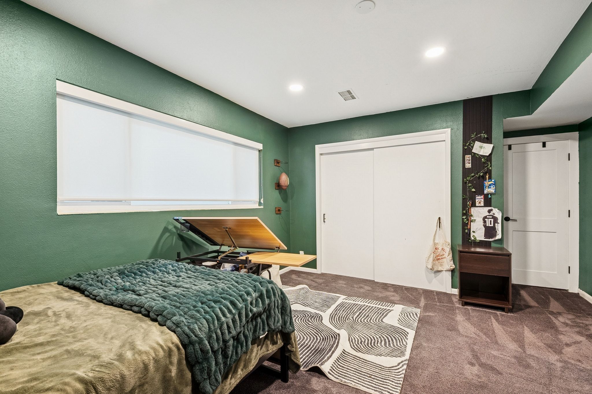 Carpeted room with a wide window featuring roller shades, built-in recessed lighting, and a two-panel sliding closet door