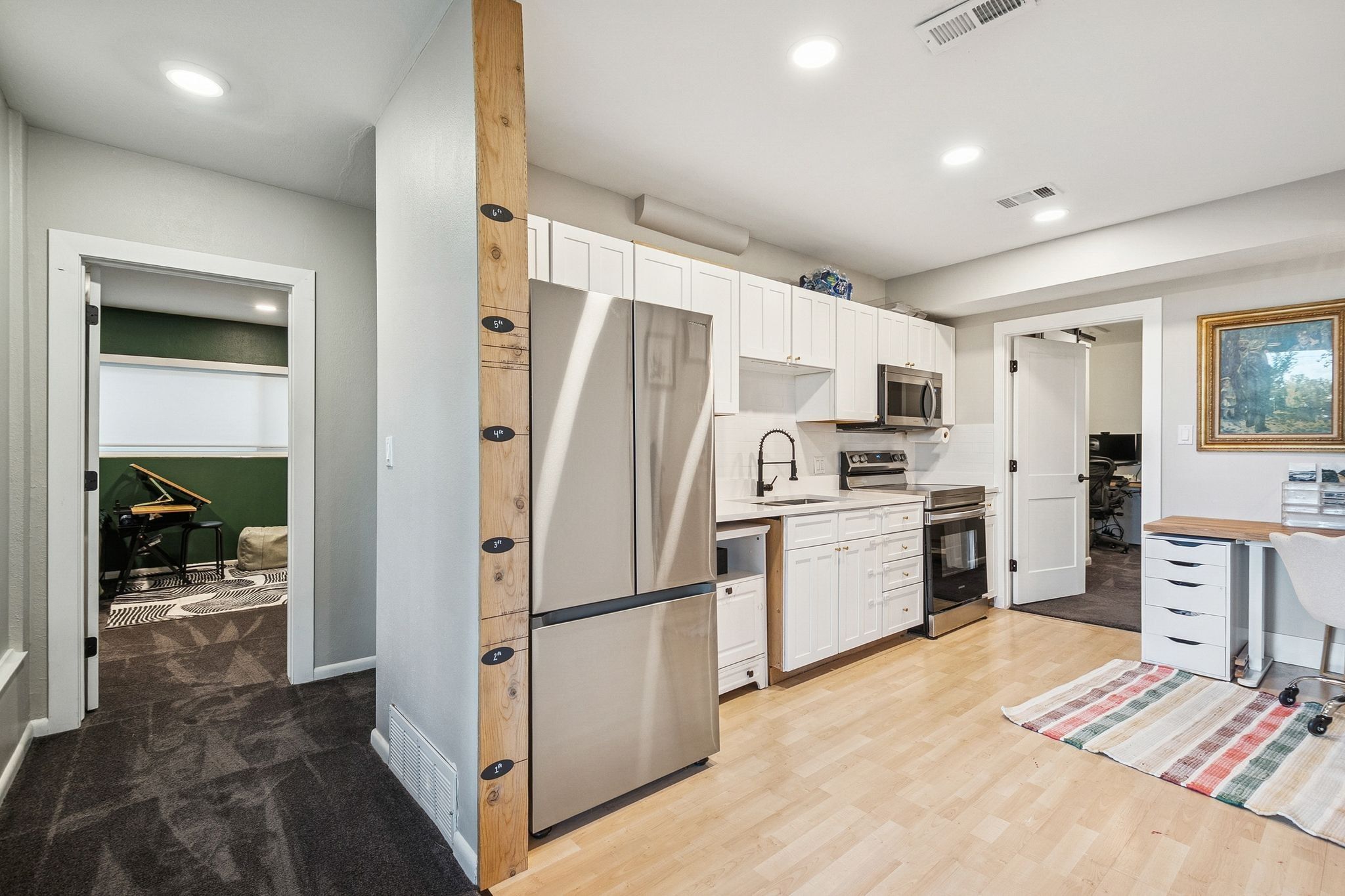 Compact kitchen area featuring white cabinetry, stainless steel appliances, and wood-finish flooring