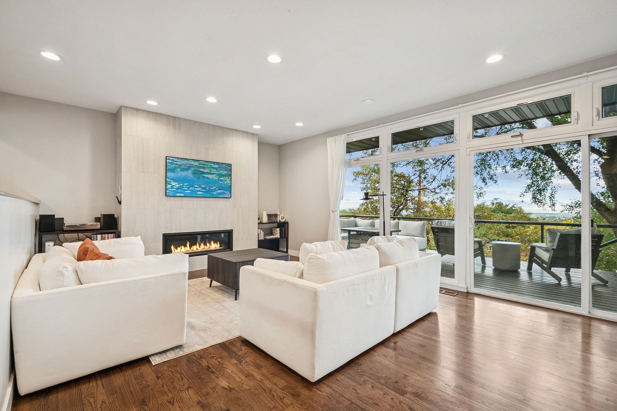 Open concept living area featuring wood-finish flooring, a contemporary fireplace with a vertical panel surround, and abundant natural light from extensive glass doors