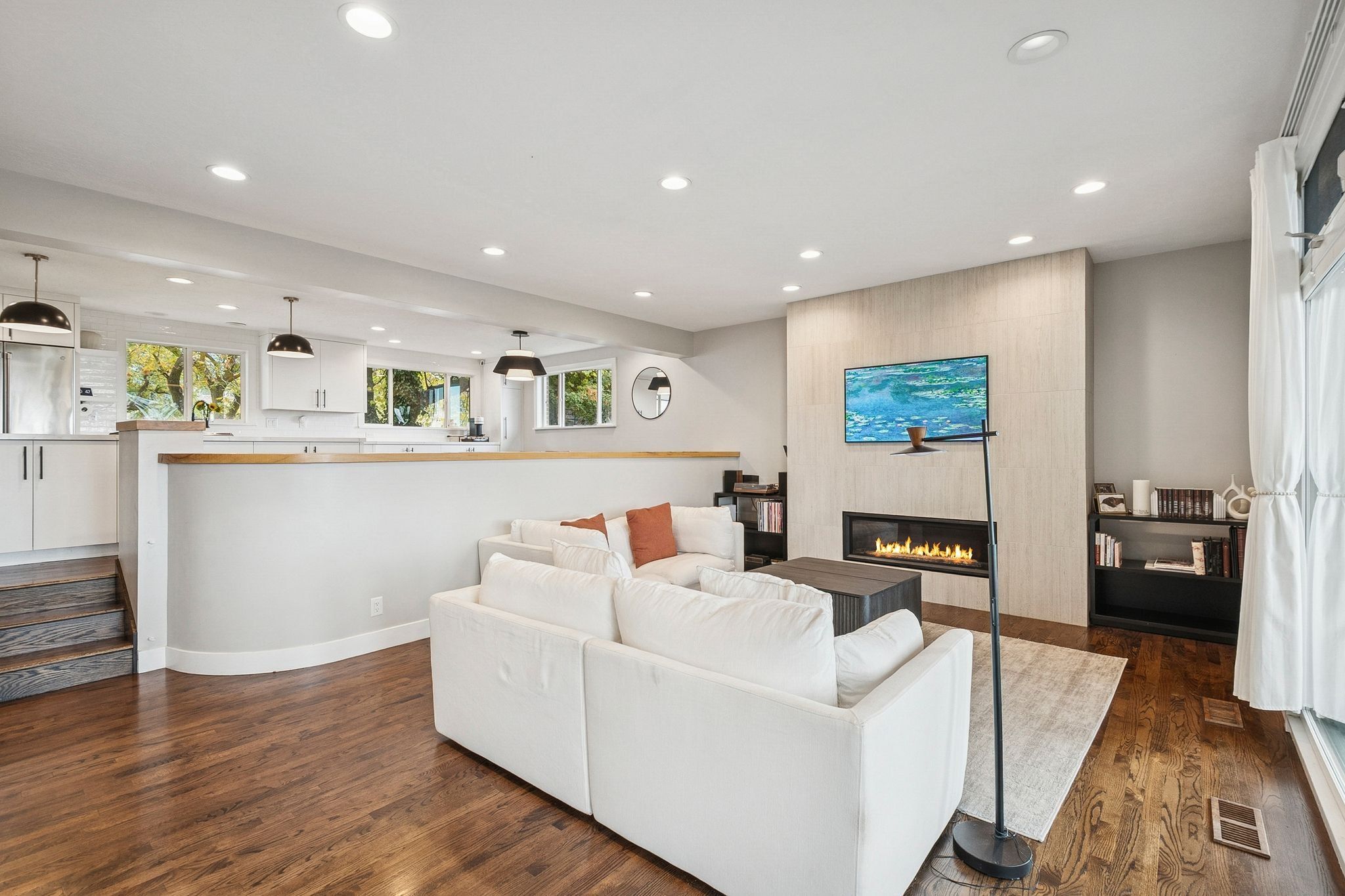 Open-concept living area featuring rich wood-finish flooring, a contemporary linear fireplace with a textured tile surround, and recessed lighting