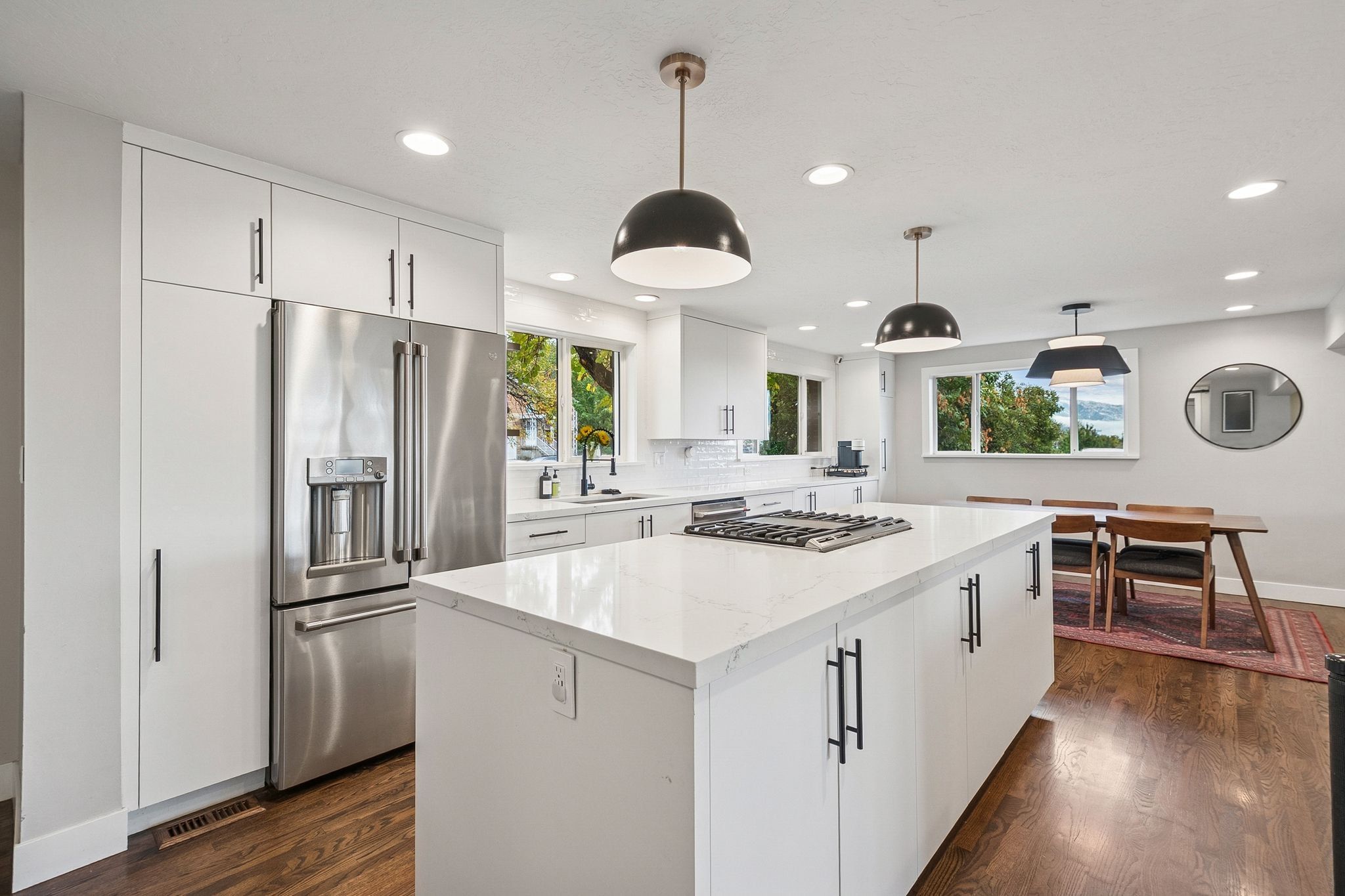 Modern kitchen featuring a large central island with a built-in gas cooktop, white perimeter cabinetry, stainless steel refrigerator, and wood-finish flooring