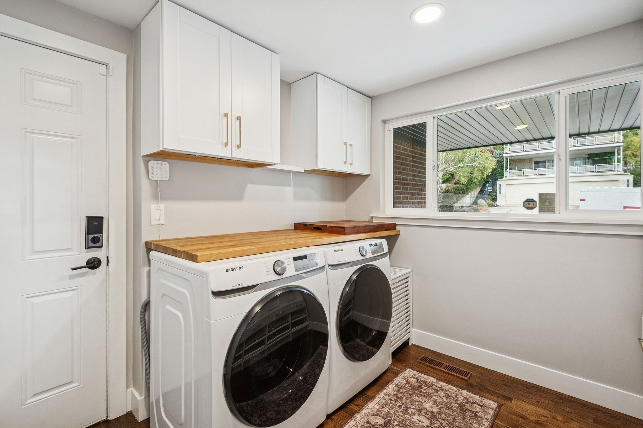 Laundry area featuring white cabinetry with gold-tone pulls, a wood-finish countertop, and dark wood-finish flooring