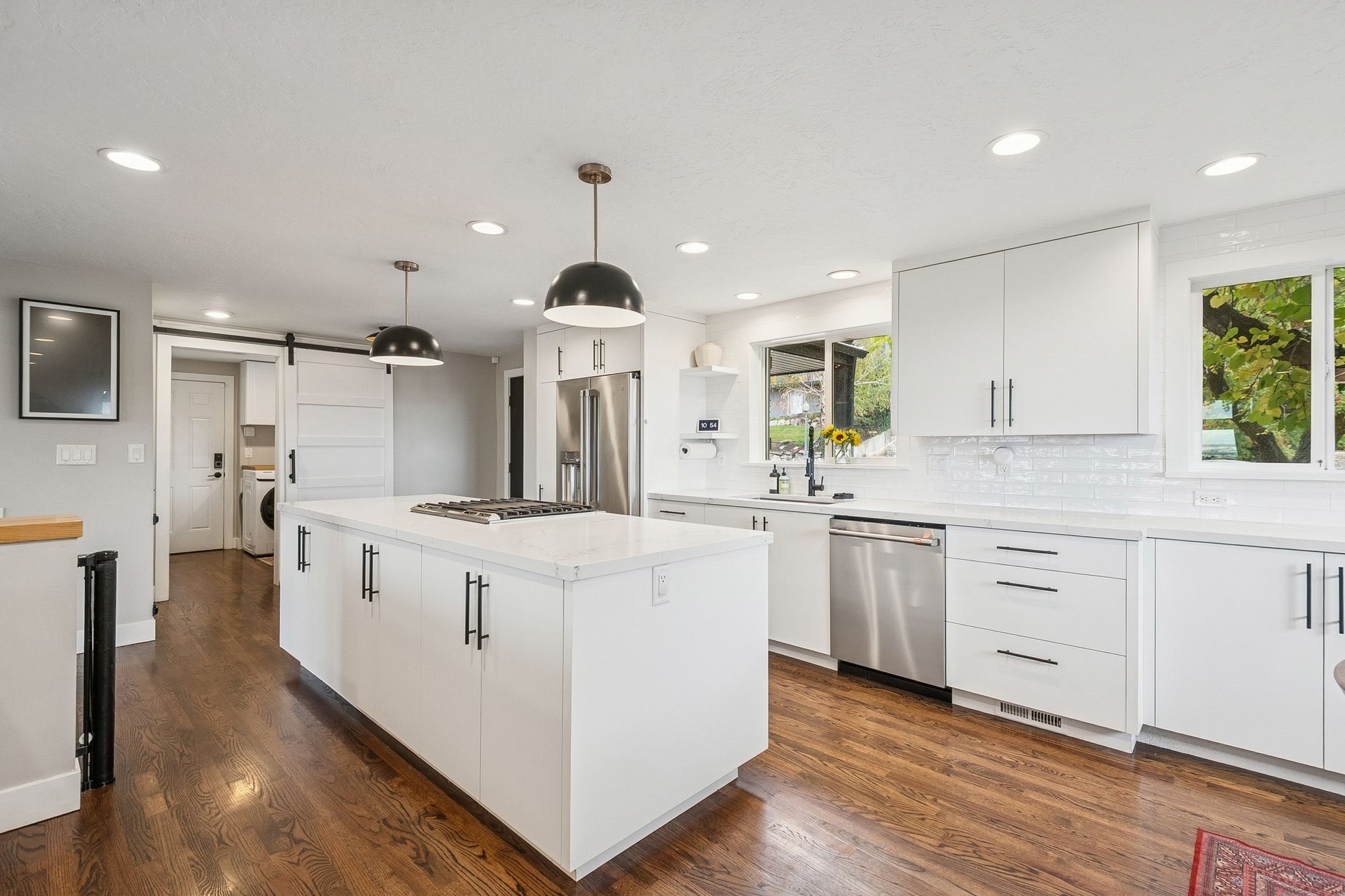 Modern kitchen featuring a large central island with a cooktop, white cabinetry, stainless steel appliances, and wood-finish flooring