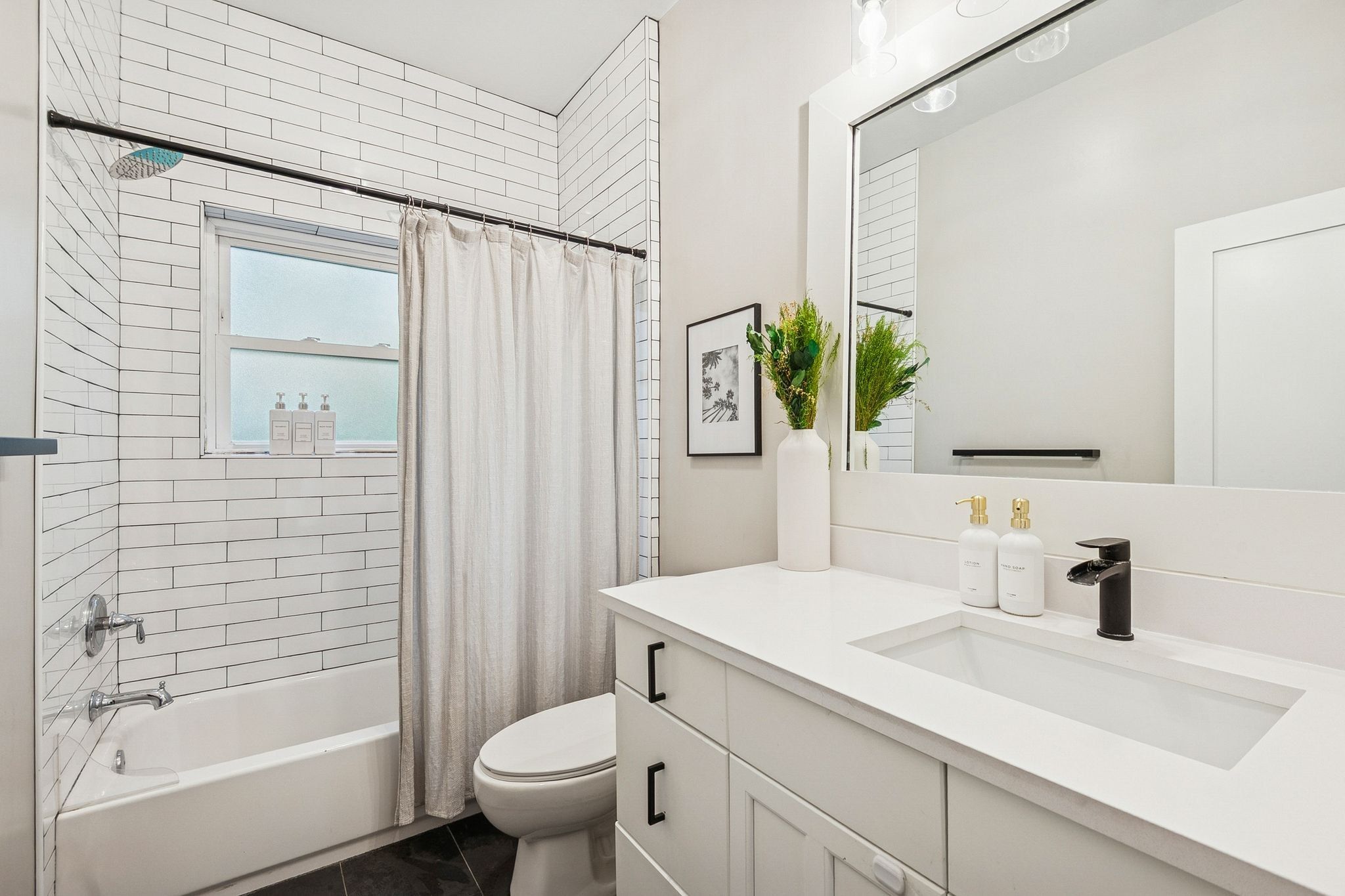 White subway tile surrounds the bathtub and shower combination, featuring a window and chrome fixtures