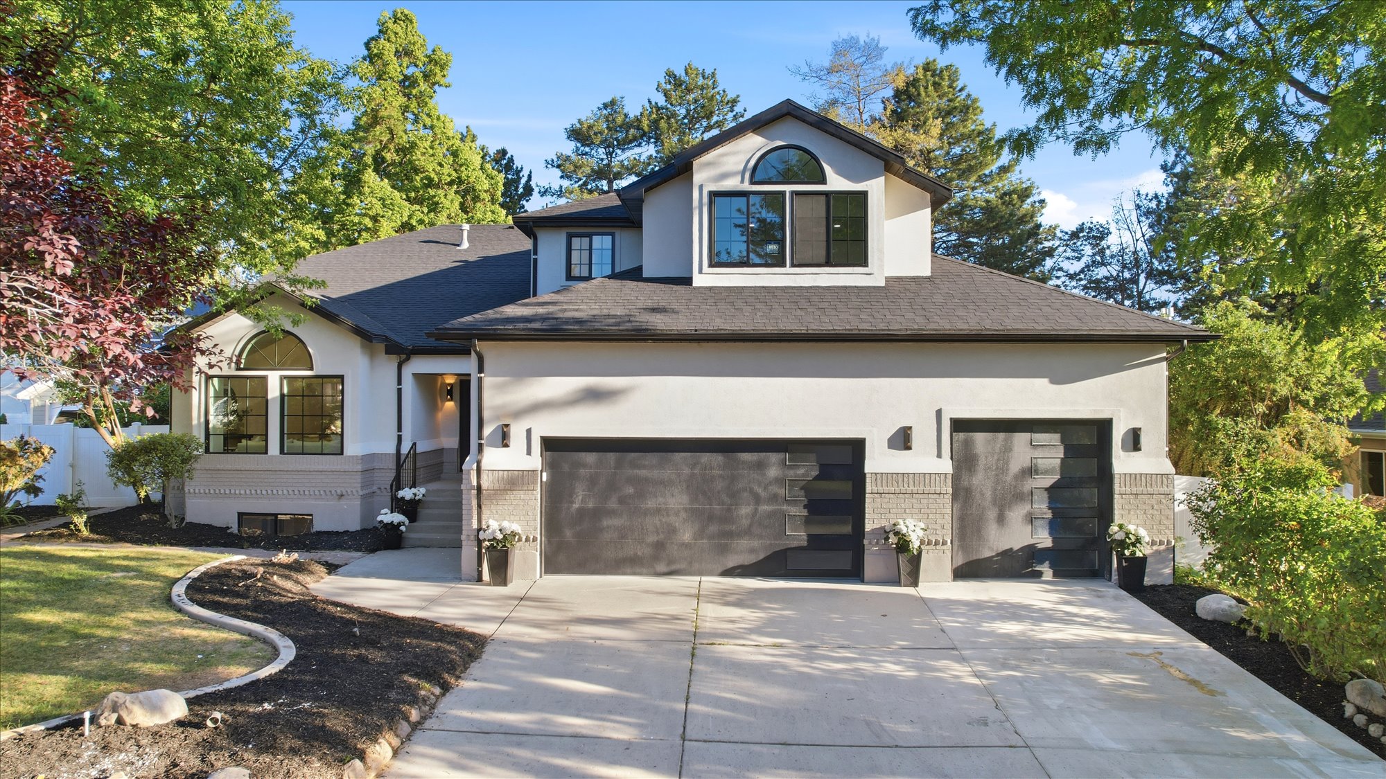 Contemporary stucco exterior featuring a two-car garage with modern doors, a prominent arched window, and landscaped front yard with a concrete driveway