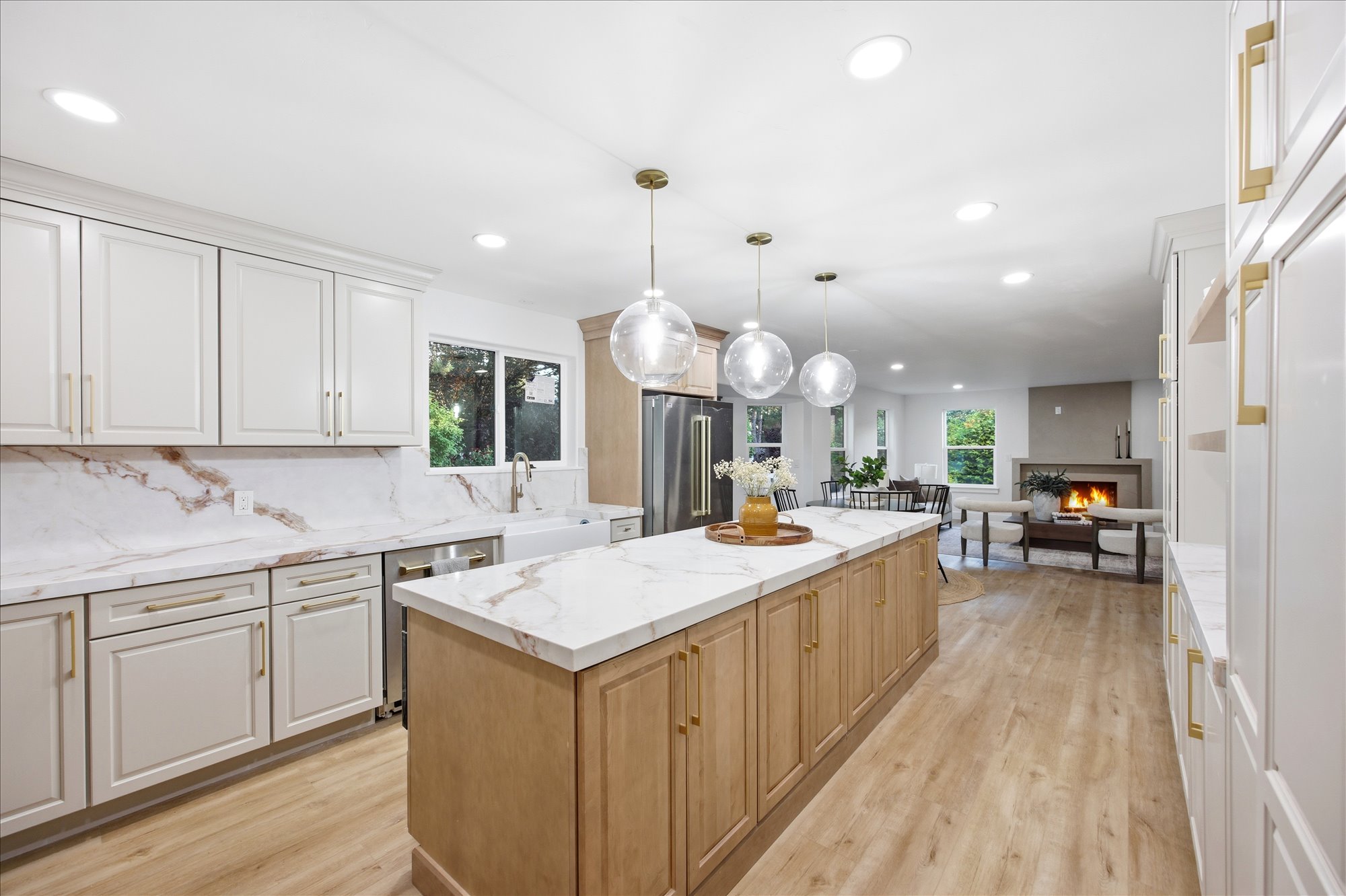 Kitchen featuring a spacious island with a light-toned countertop, pendant lighting, shaker-style cabinetry, a farmhouse sink, and wood-finish flooring