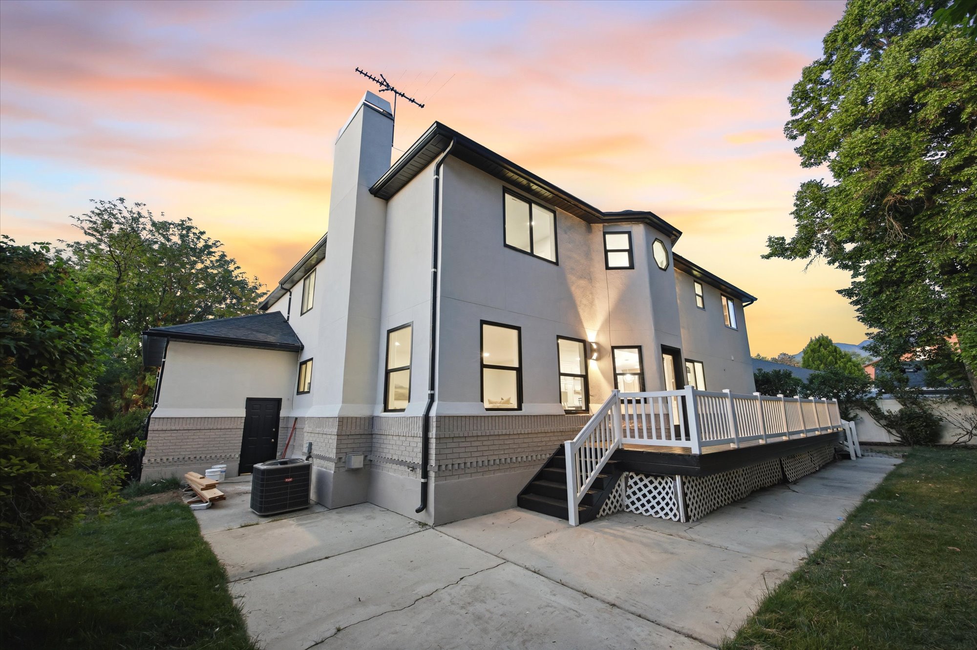 Rear exterior featuring a large elevated deck with white railing, stucco siding, and a brick foundation