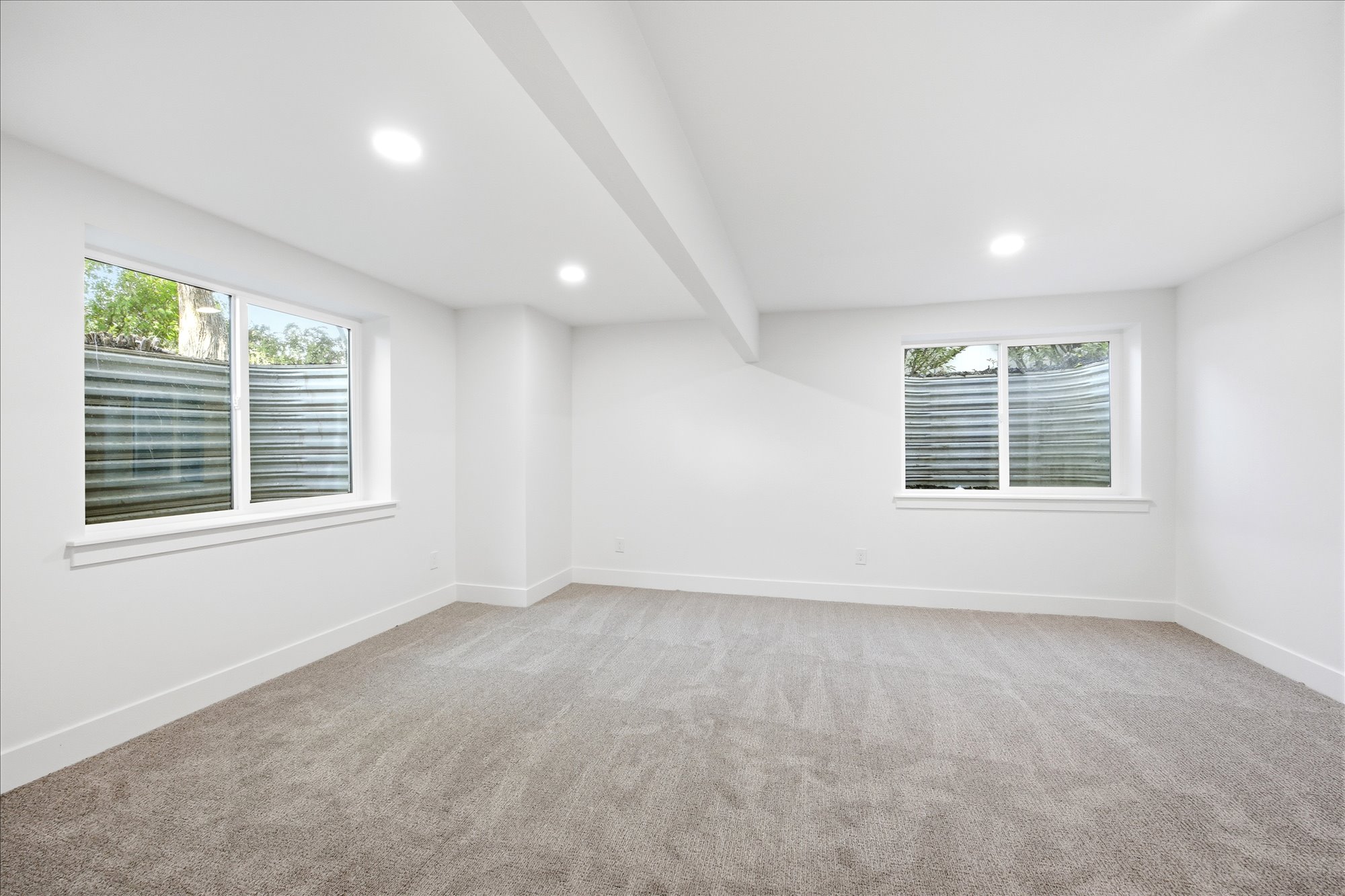 Spacious interior room featuring light gray carpeting, white walls, and bright recessed lighting