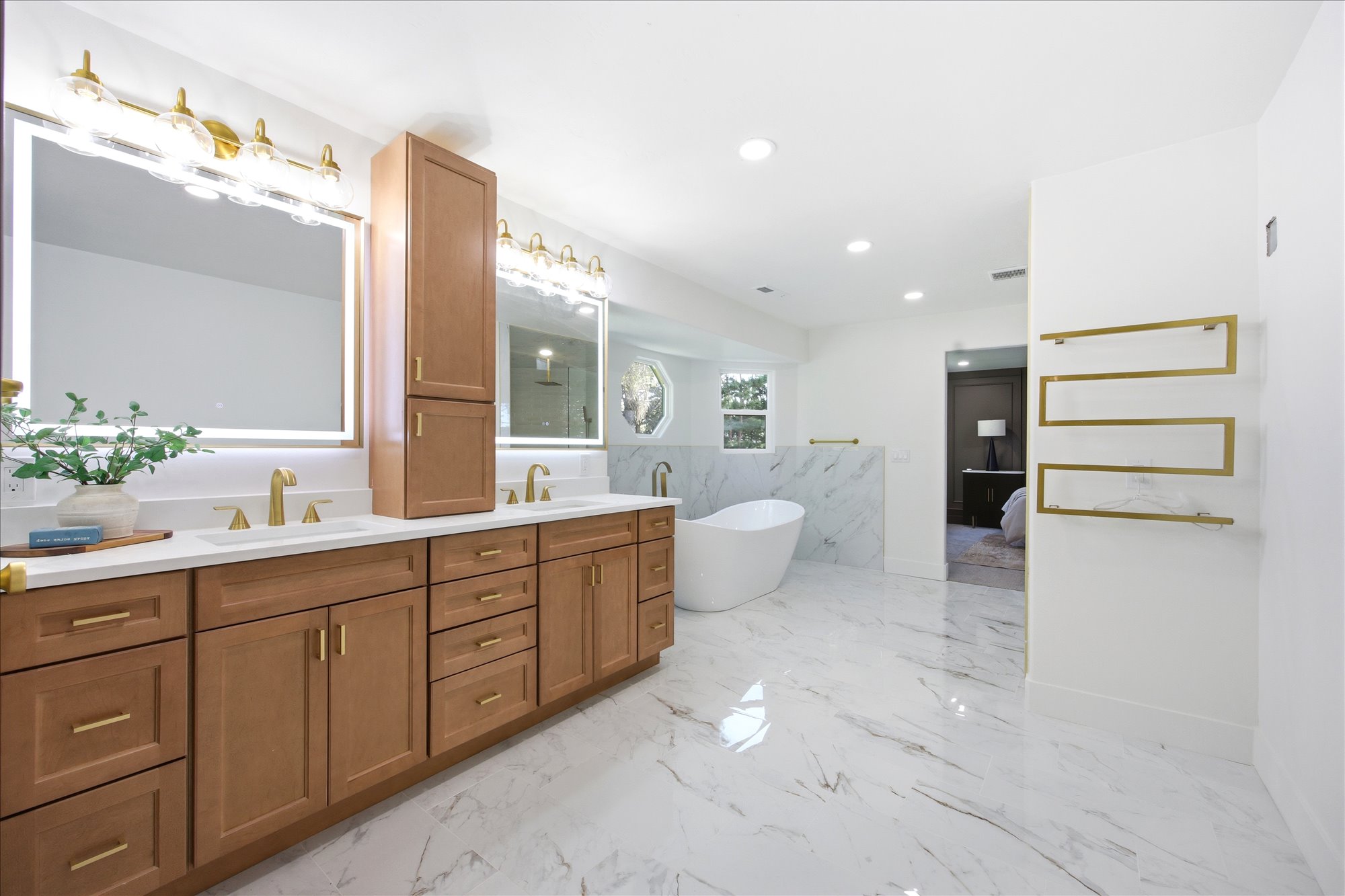 Spacious bathroom featuring a dual vanity with light wood cabinetry, white countertops, and gold-finish fixtures