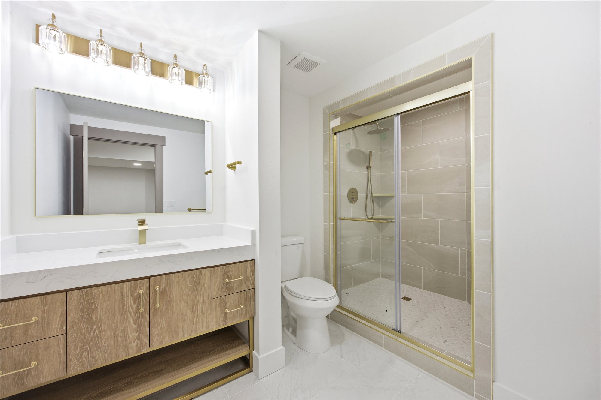 Bathroom featuring a wood-finish double vanity with white countertop, brass fixtures, and an illuminated mirror
