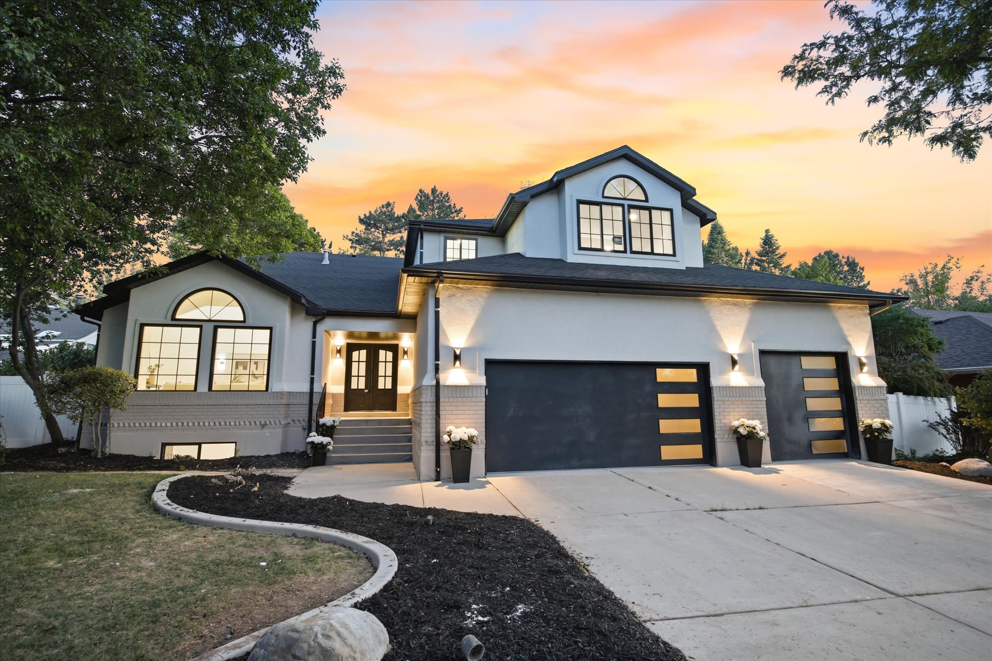 Modern stucco exterior featuring a two-car garage with contemporary glass-paneled doors, arched windows, and a concrete driveway