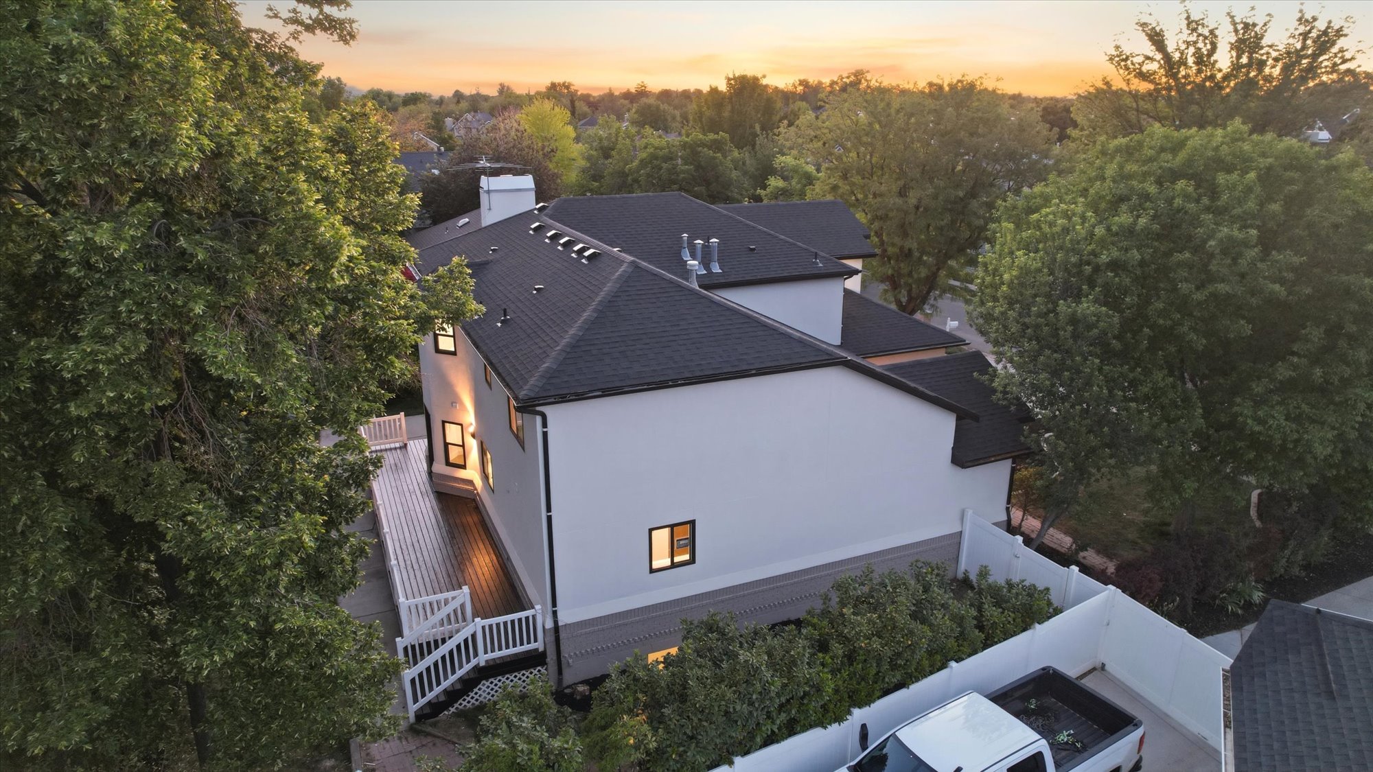 Contemporary white exterior with dark-framed windows, a dark shingled roof, and a multi-level wood deck featuring white railings and stairs