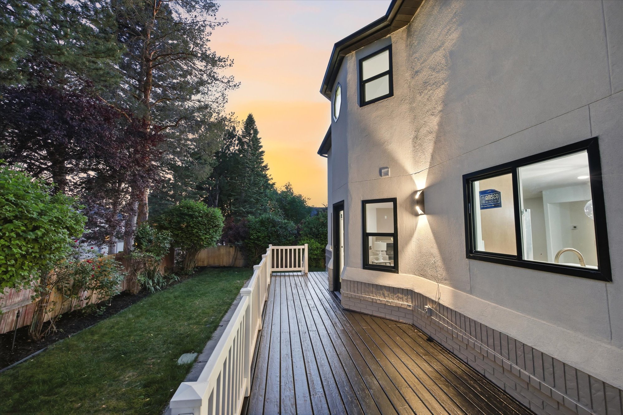 Spacious outdoor deck with wood-finish planks, white railing, and exterior wall sconce lighting