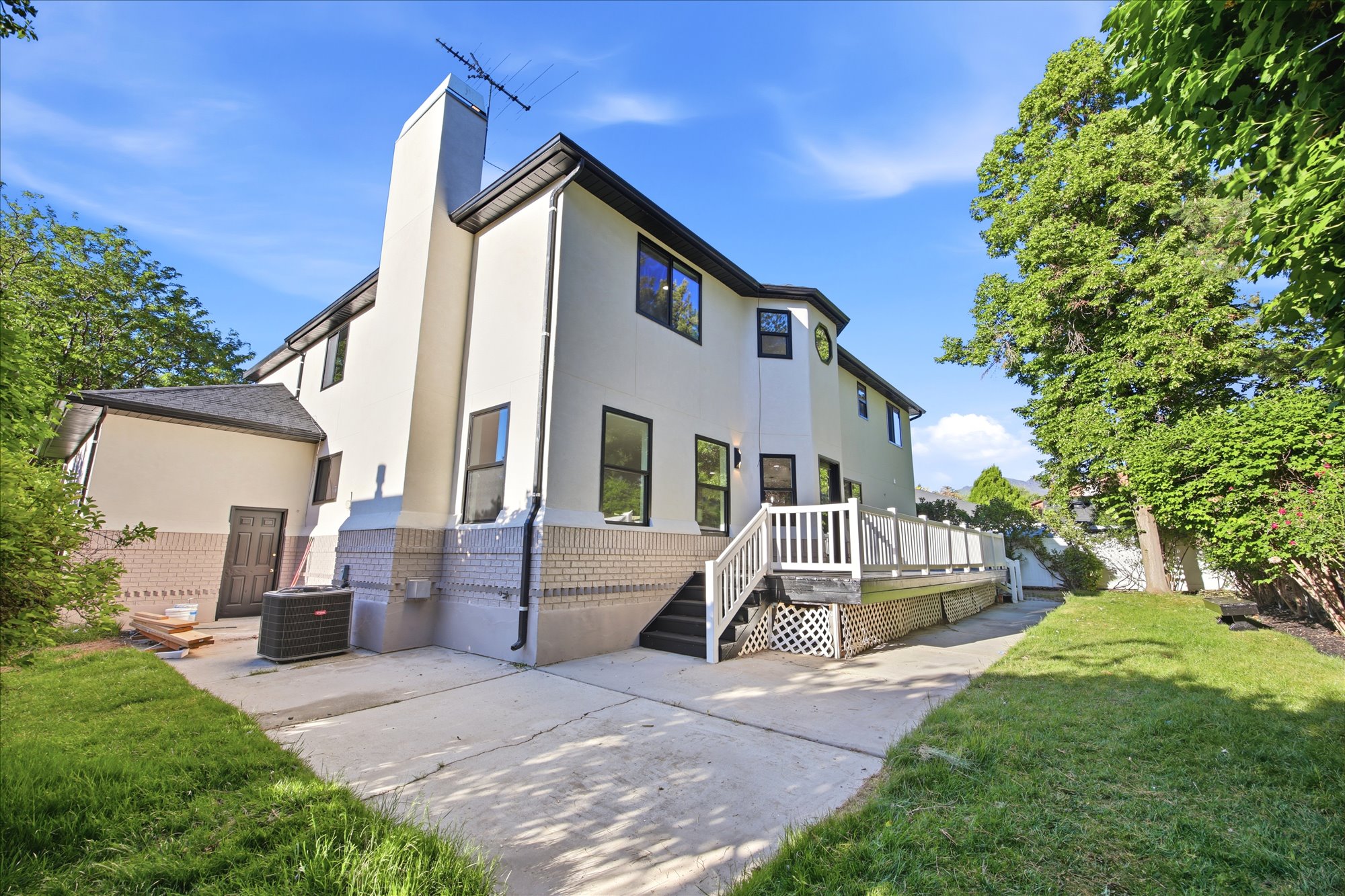 Rear exterior featuring a multi-level deck with white railings, a concrete patio, and a grass lawn
