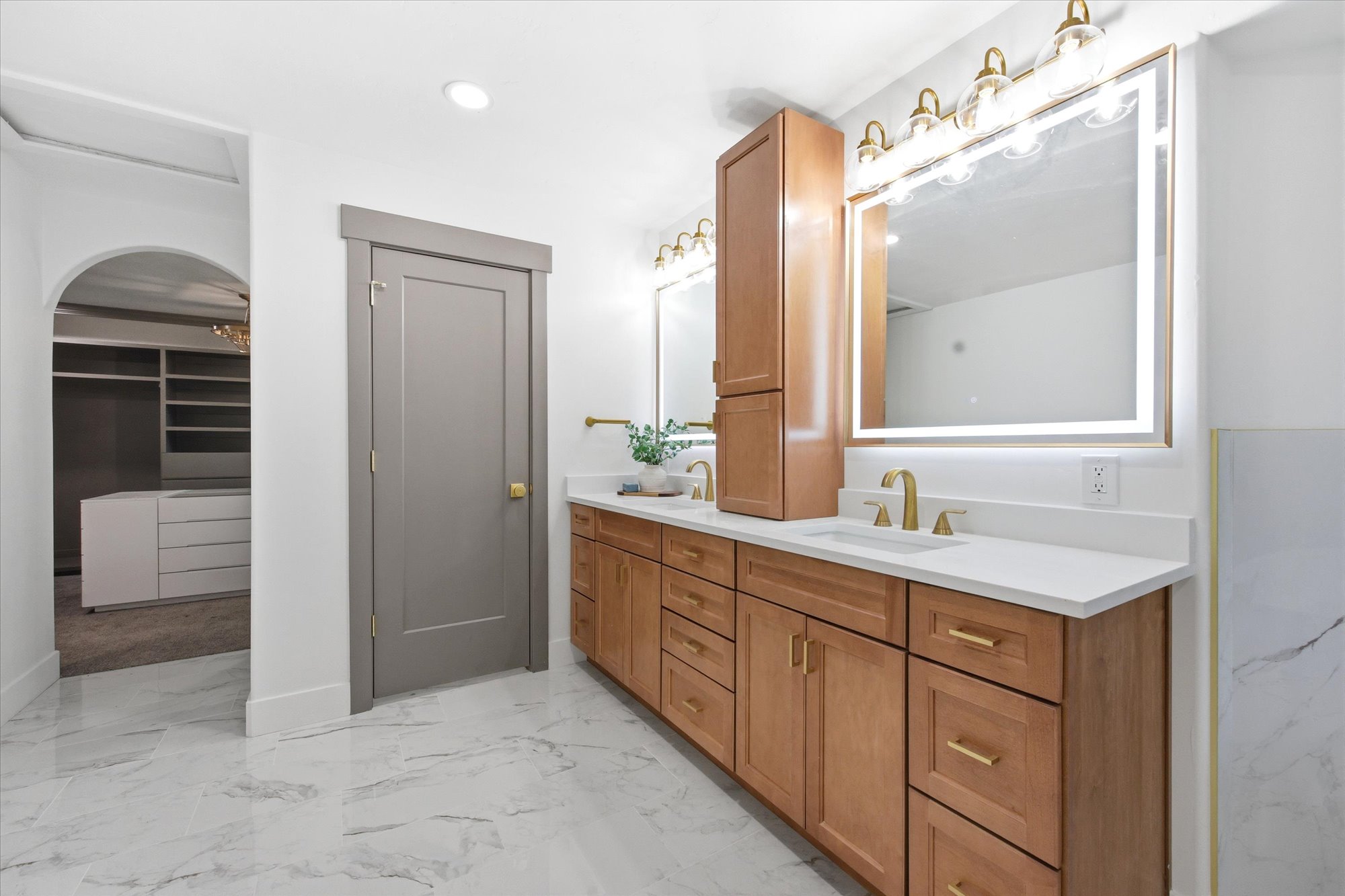 Dual vanity with light wood-finish cabinetry, white countertops, and gold-toned fixtures