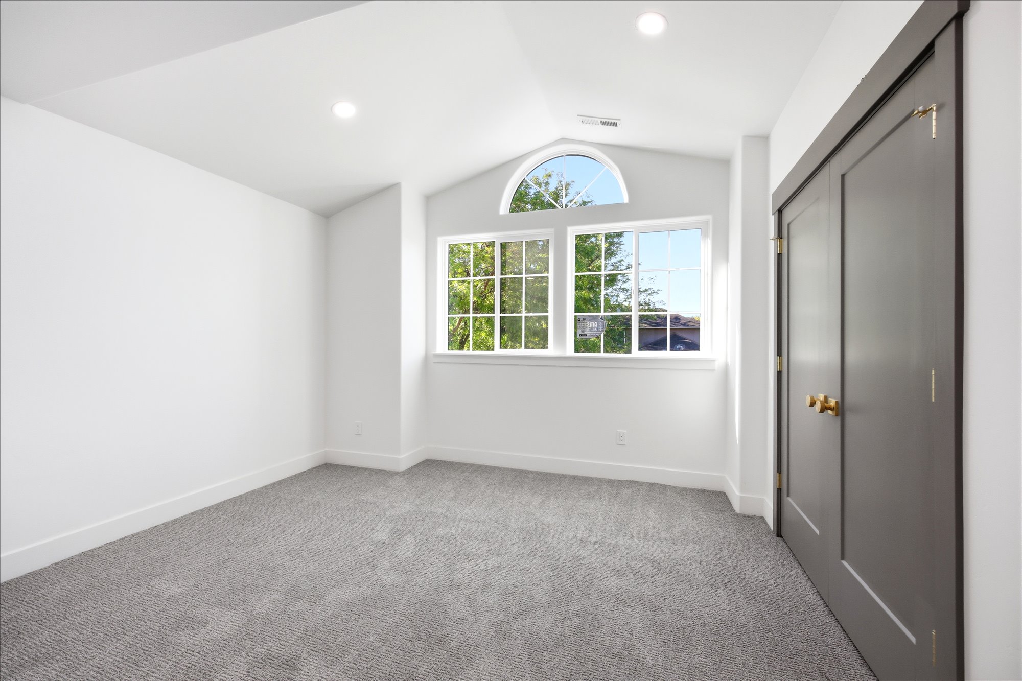 Carpeted room featuring a vaulted ceiling with recessed lighting, a large arched window, and a dark-paneled closet with brass hardware