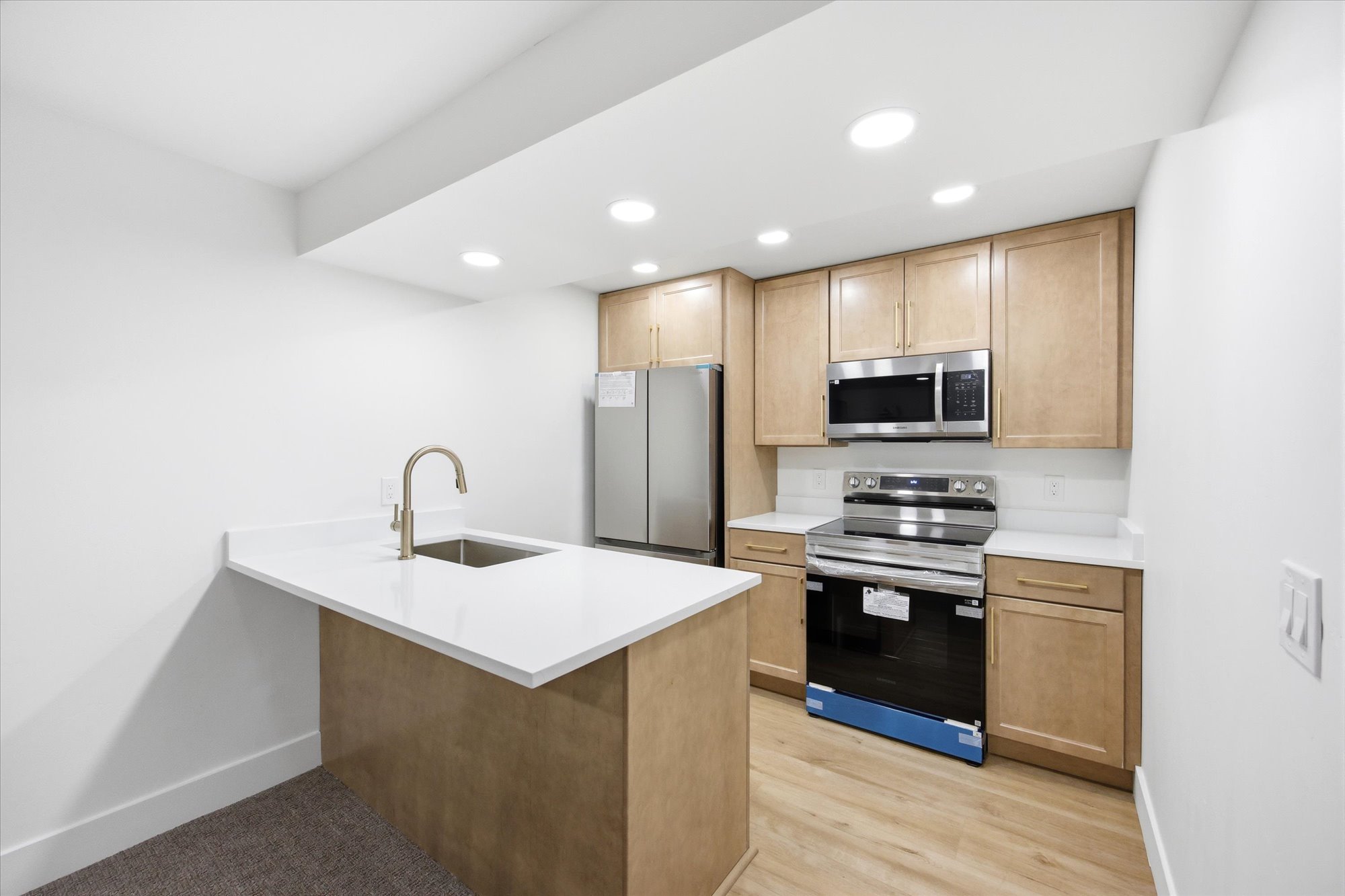 Modern kitchen featuring light wood-finish cabinetry, stainless steel appliances, white countertops, and recessed lighting