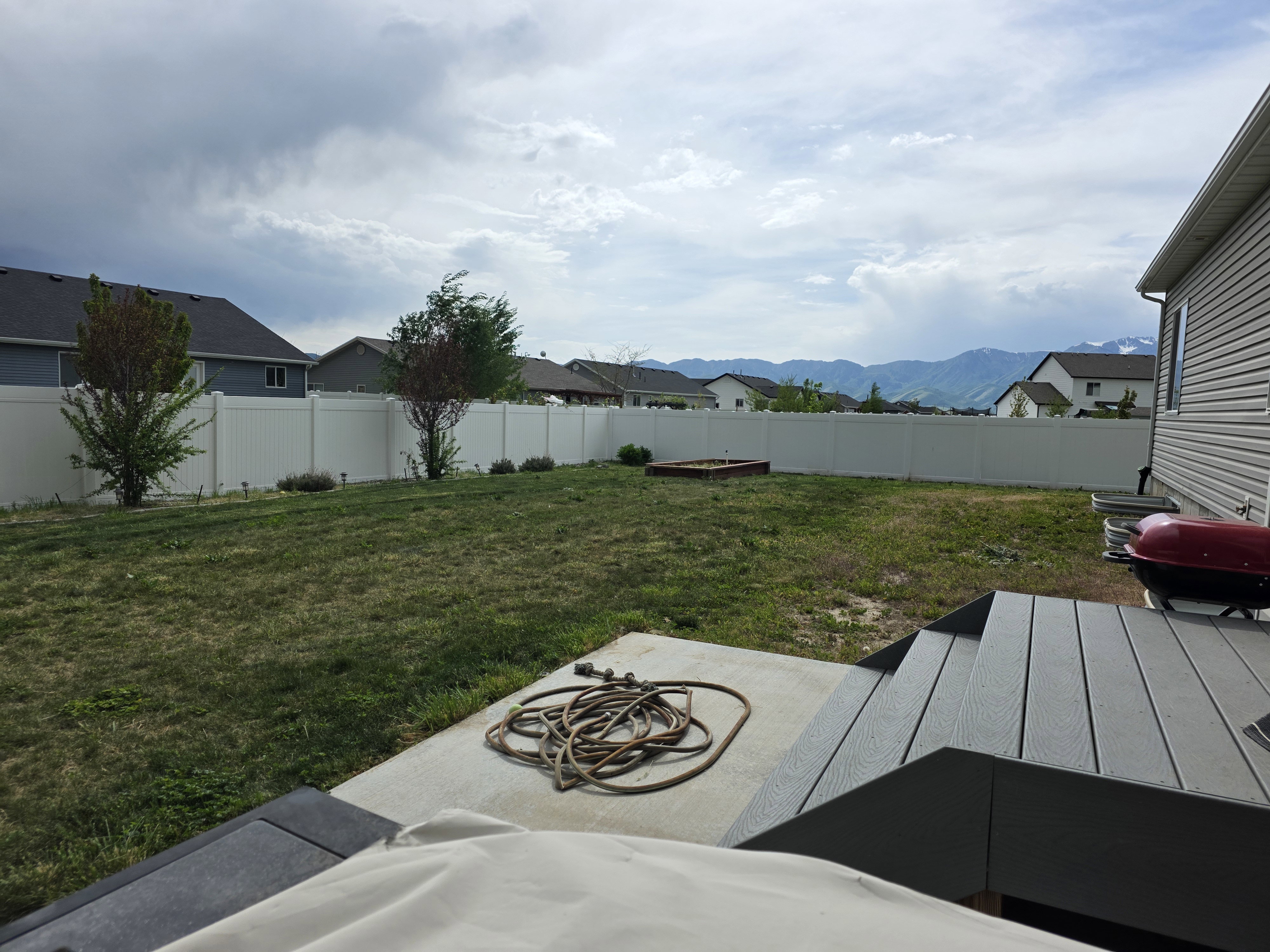 Expansive backyard featuring a privacy fence, mature trees, concrete patio, and composite decking