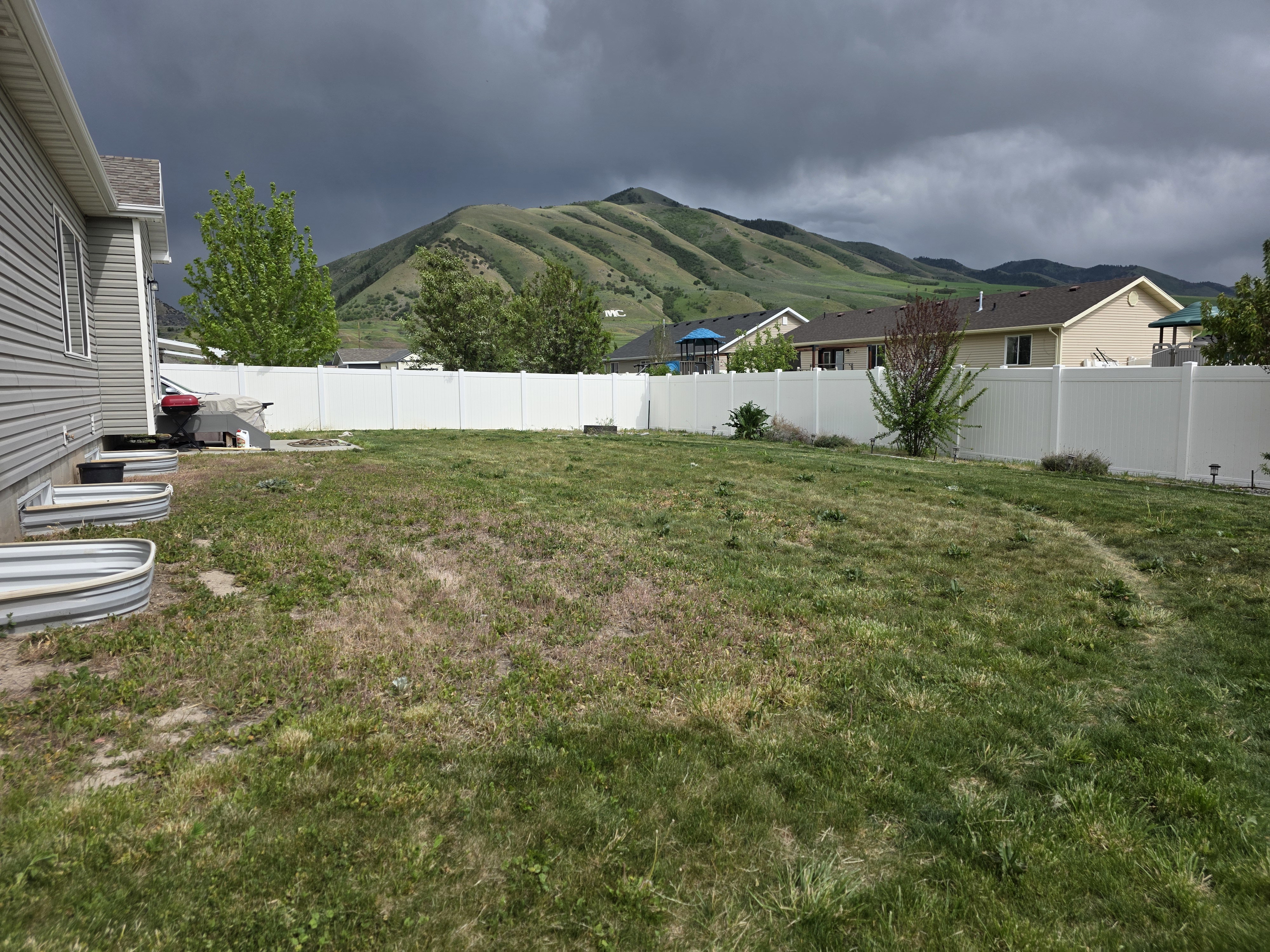 Expansive backyard featuring a white privacy fence, mountain backdrop, and side yard access with window wells