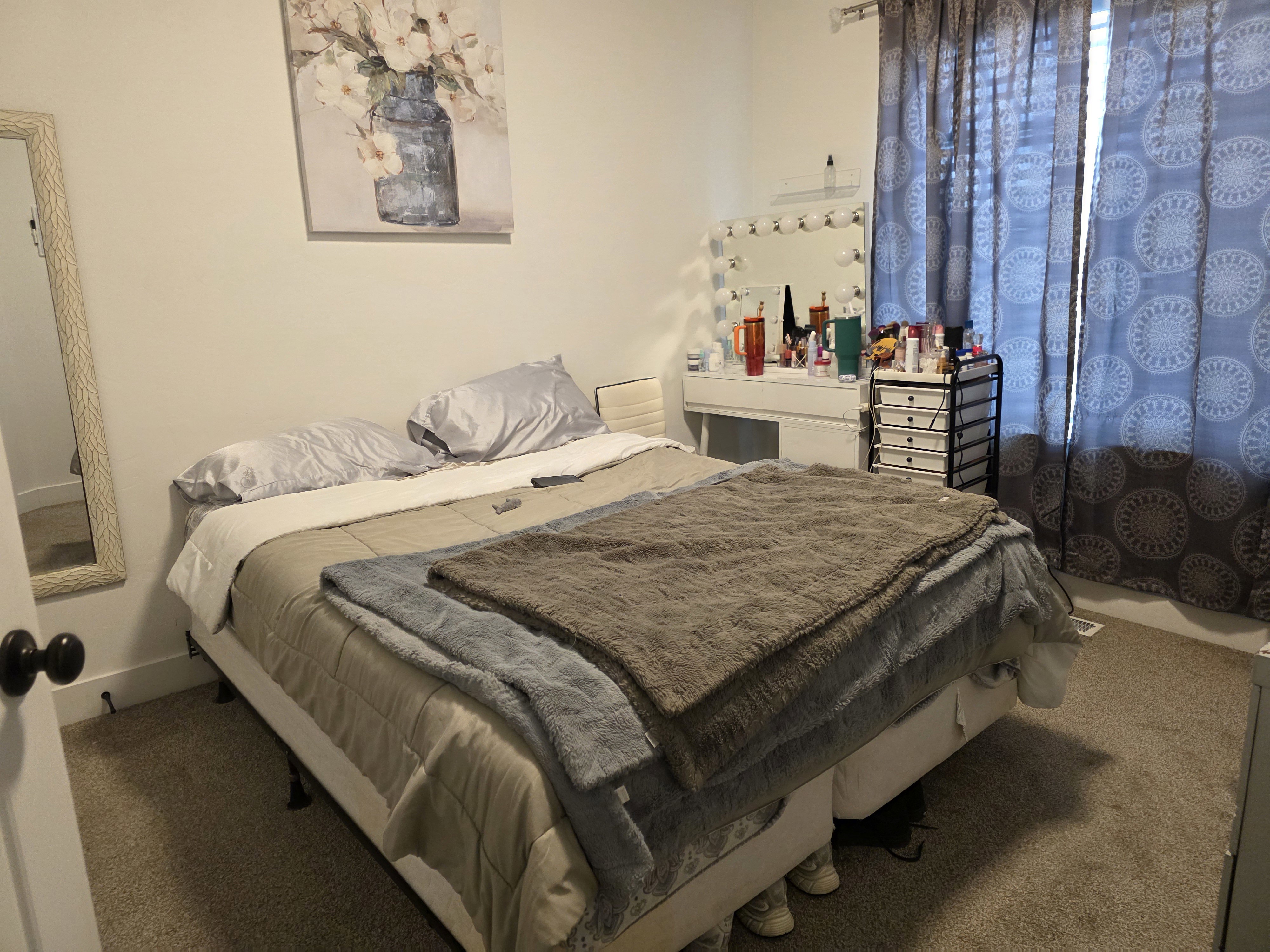 Carpeted bedroom with neutral wall tones and a window featuring patterned curtains