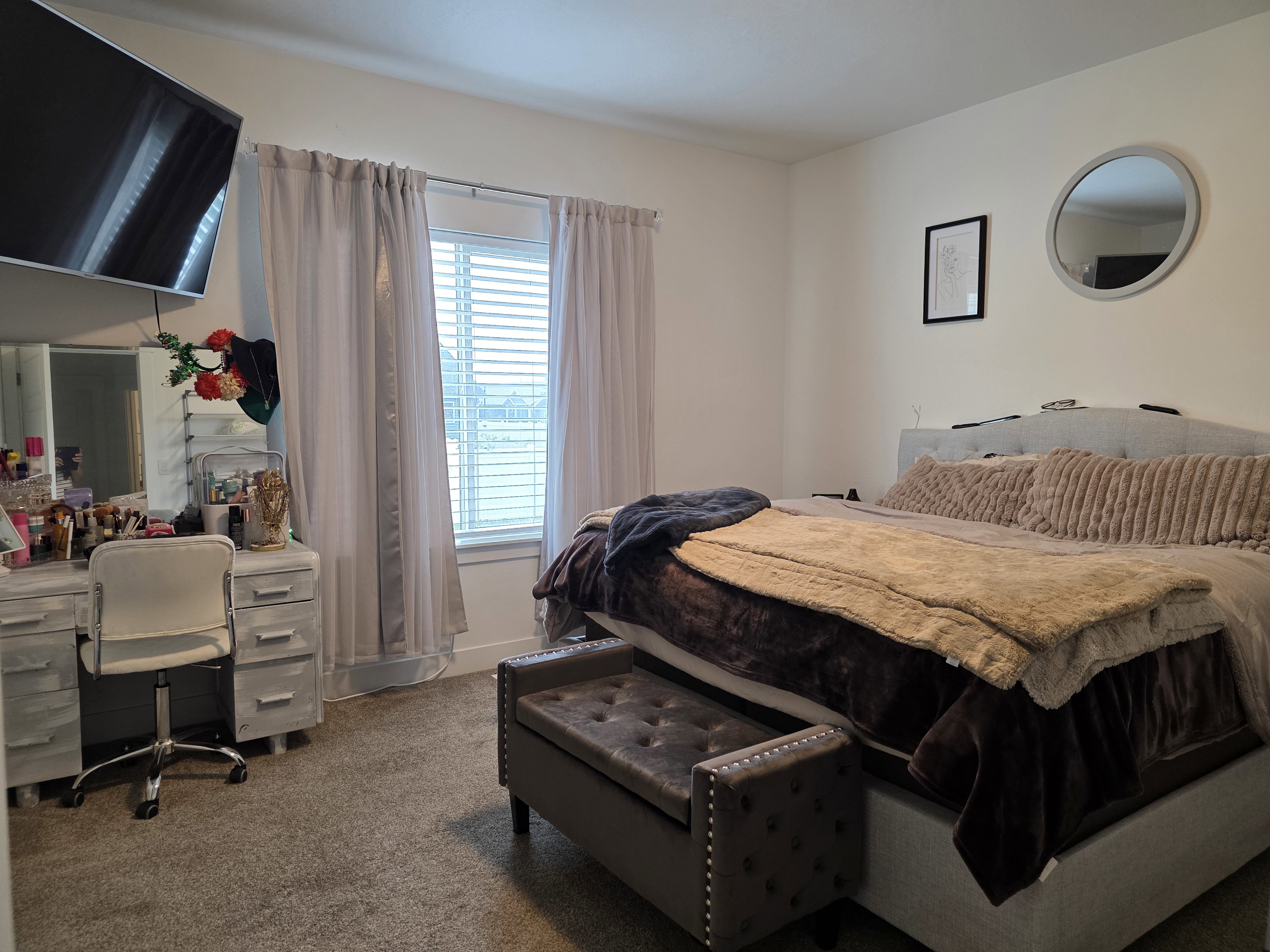 Bright room featuring a window with blinds and sheer curtains, carpeted flooring, and a wall-mounted flat-screen television