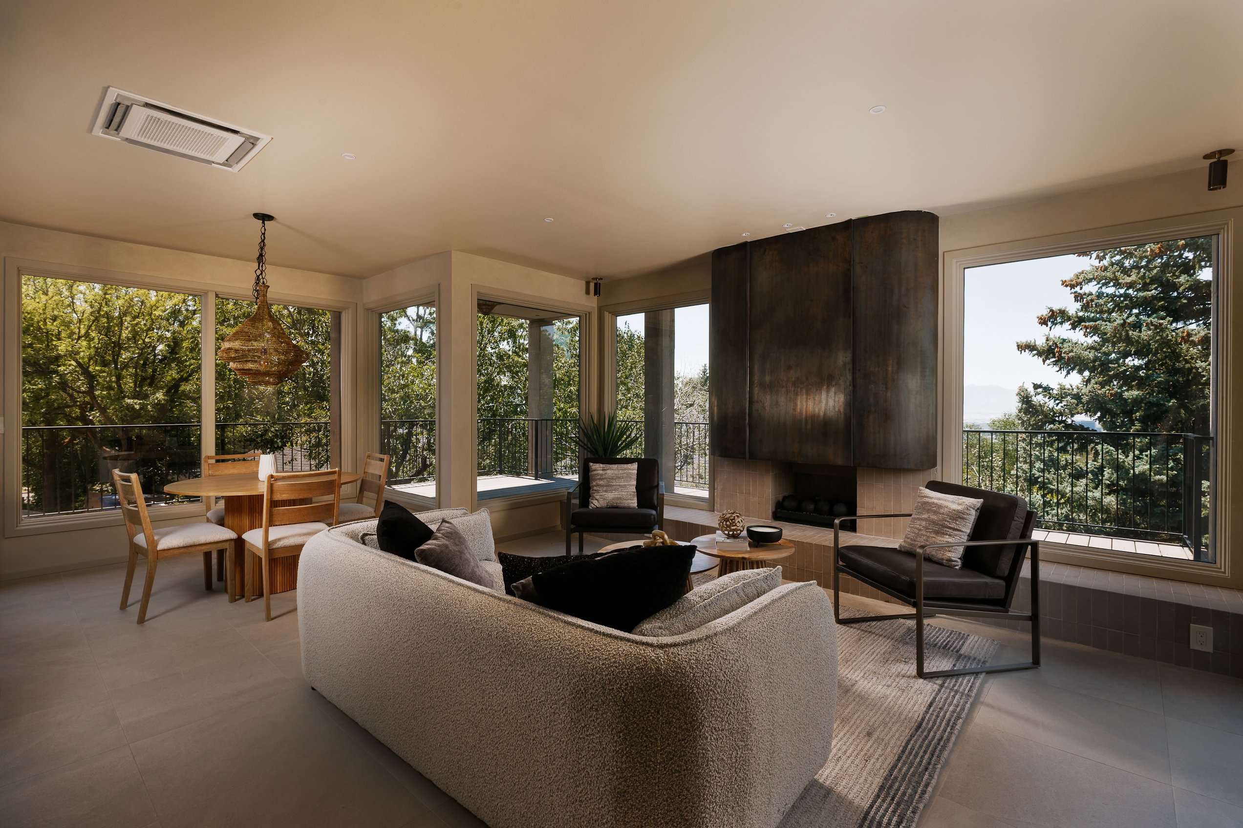 Open-concept living area with expansive windows, a curved metal fireplace surround, and wood-finish flooring