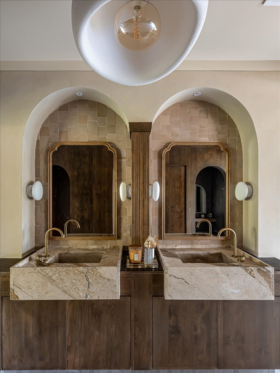 Dual stone vessel sinks with gold-finish faucets atop dark wood cabinetry