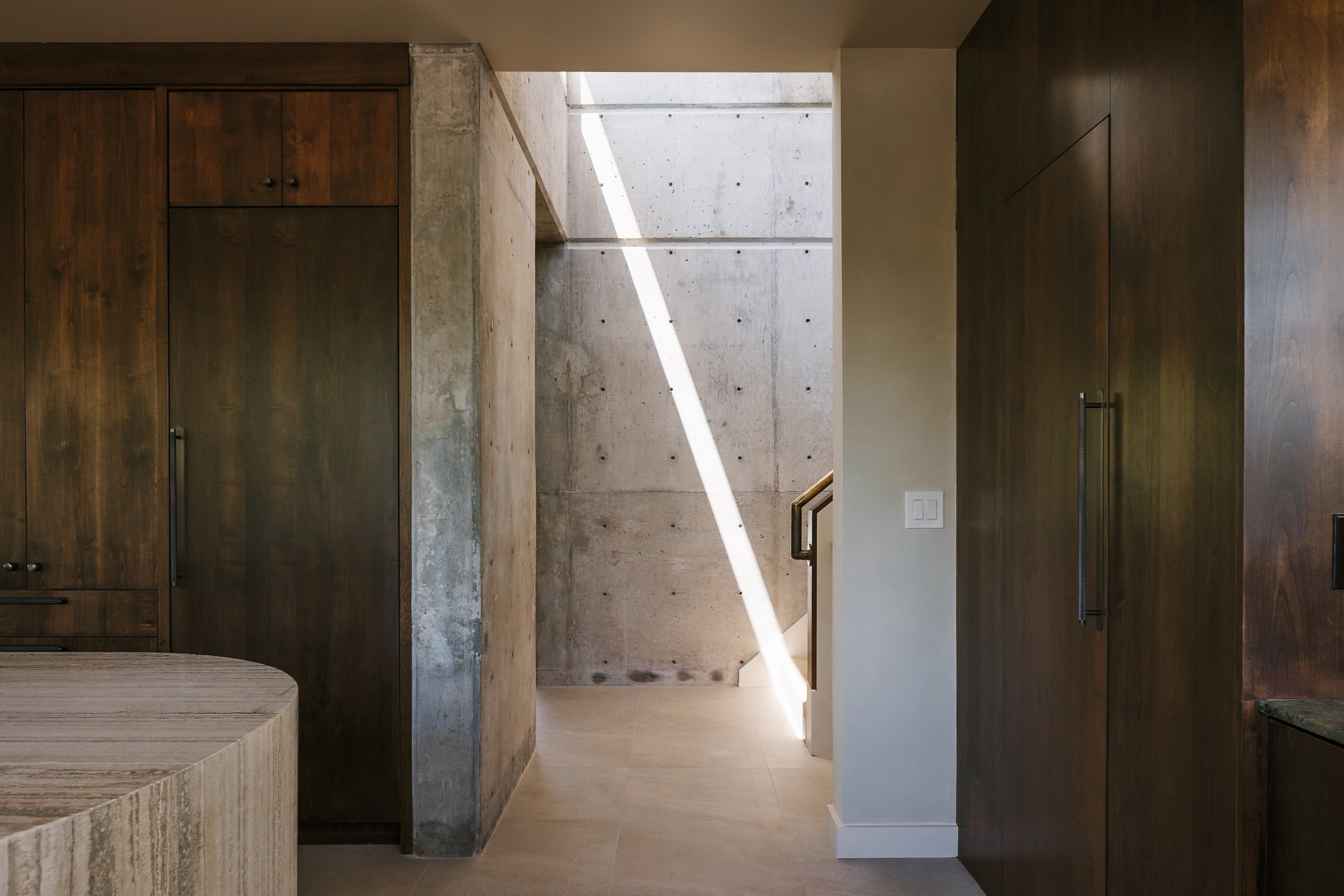 Architectural concrete wall with integrated skylight, wood-finish cabinetry, and a curved island featuring a stone-look finish