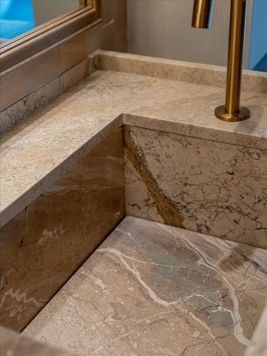 Integrated stone countertop and sink with natural veining, featuring a contemporary gold-tone faucet and a framed mirror