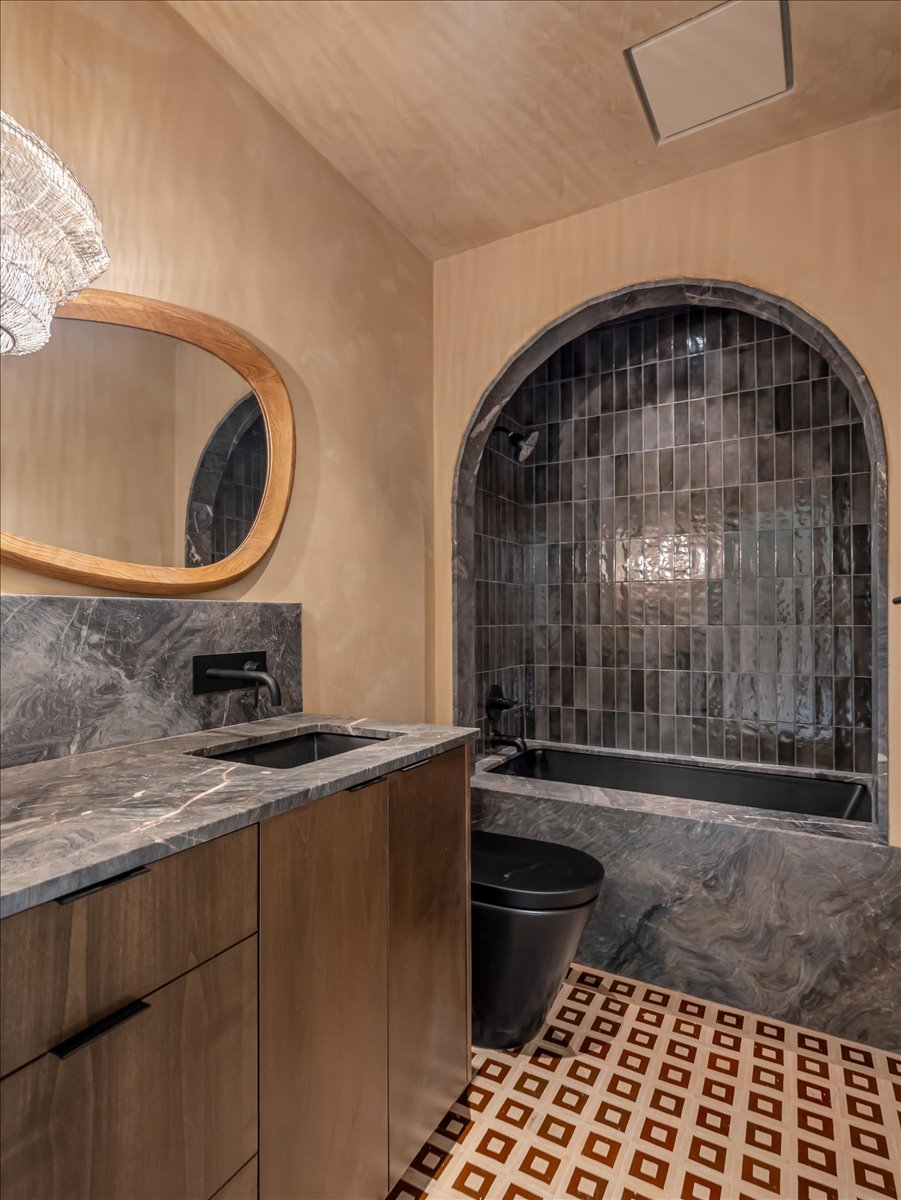 Bathroom featuring an arched alcove with dark subway tile, an integrated black bathtub, and a black toilet