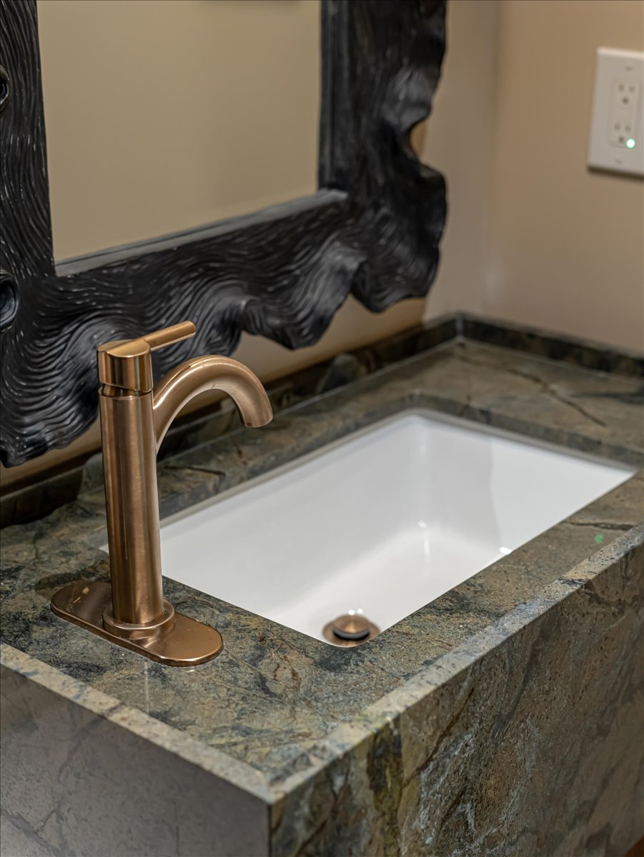 Rectangular undermount sink set into a green textured stone vanity with a bronze-finish faucet